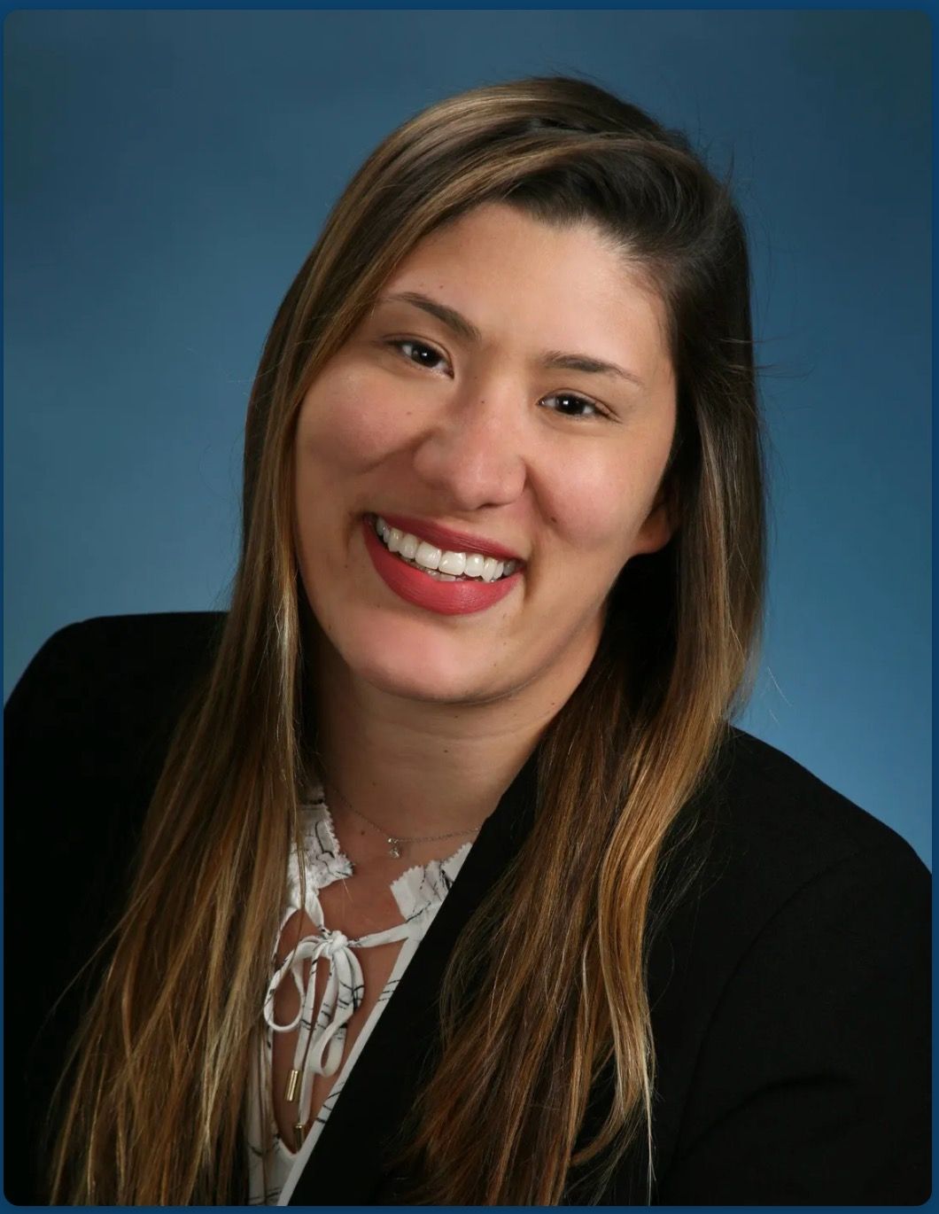 Smiling woman in a black blazer against a blue studio background