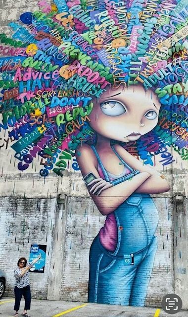 A woman is standing in front of a mural of a girl with words on her hair