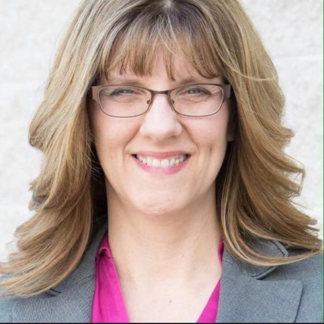 A woman wearing glasses and a pink shirt smiles for the camera