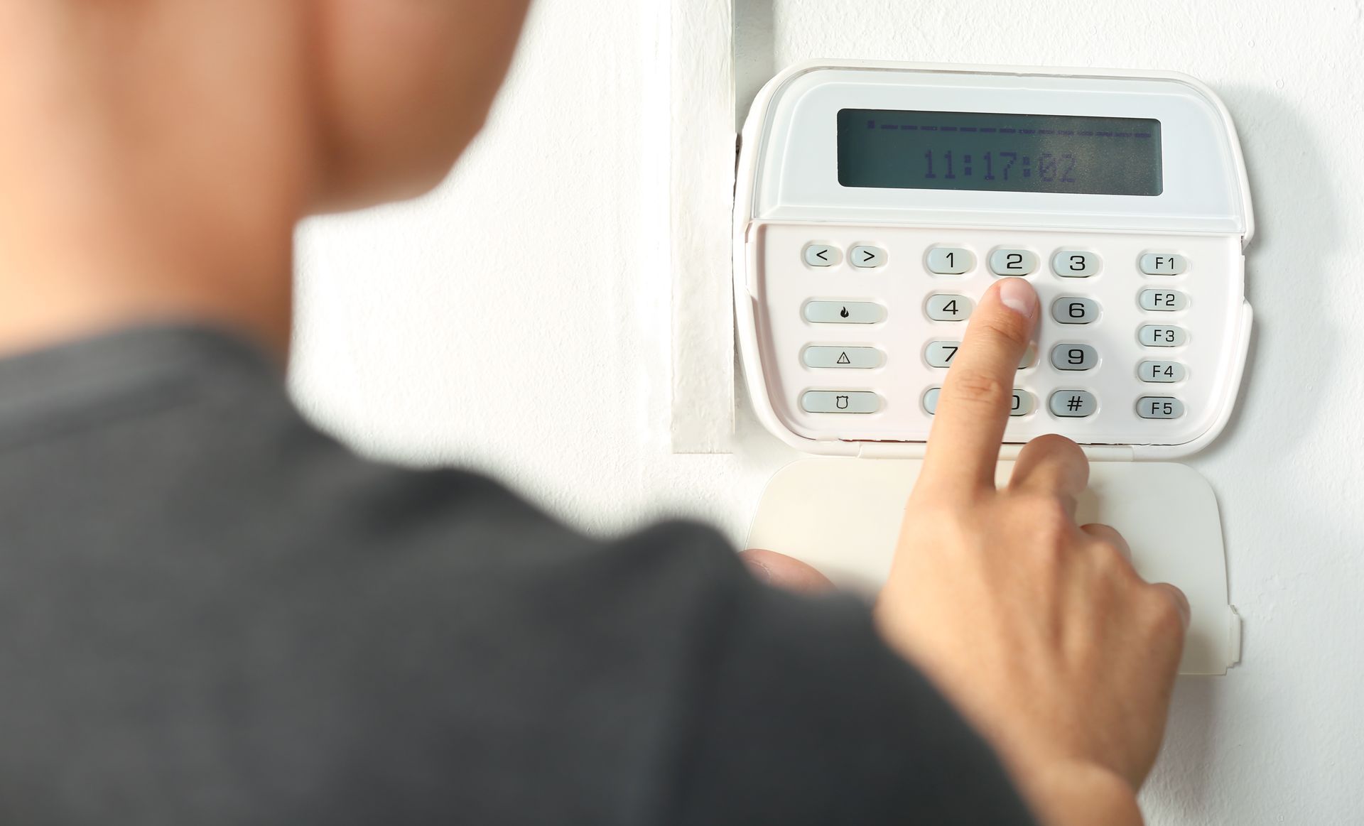 Person entering code on a white security system keypad mounted on a white wall.