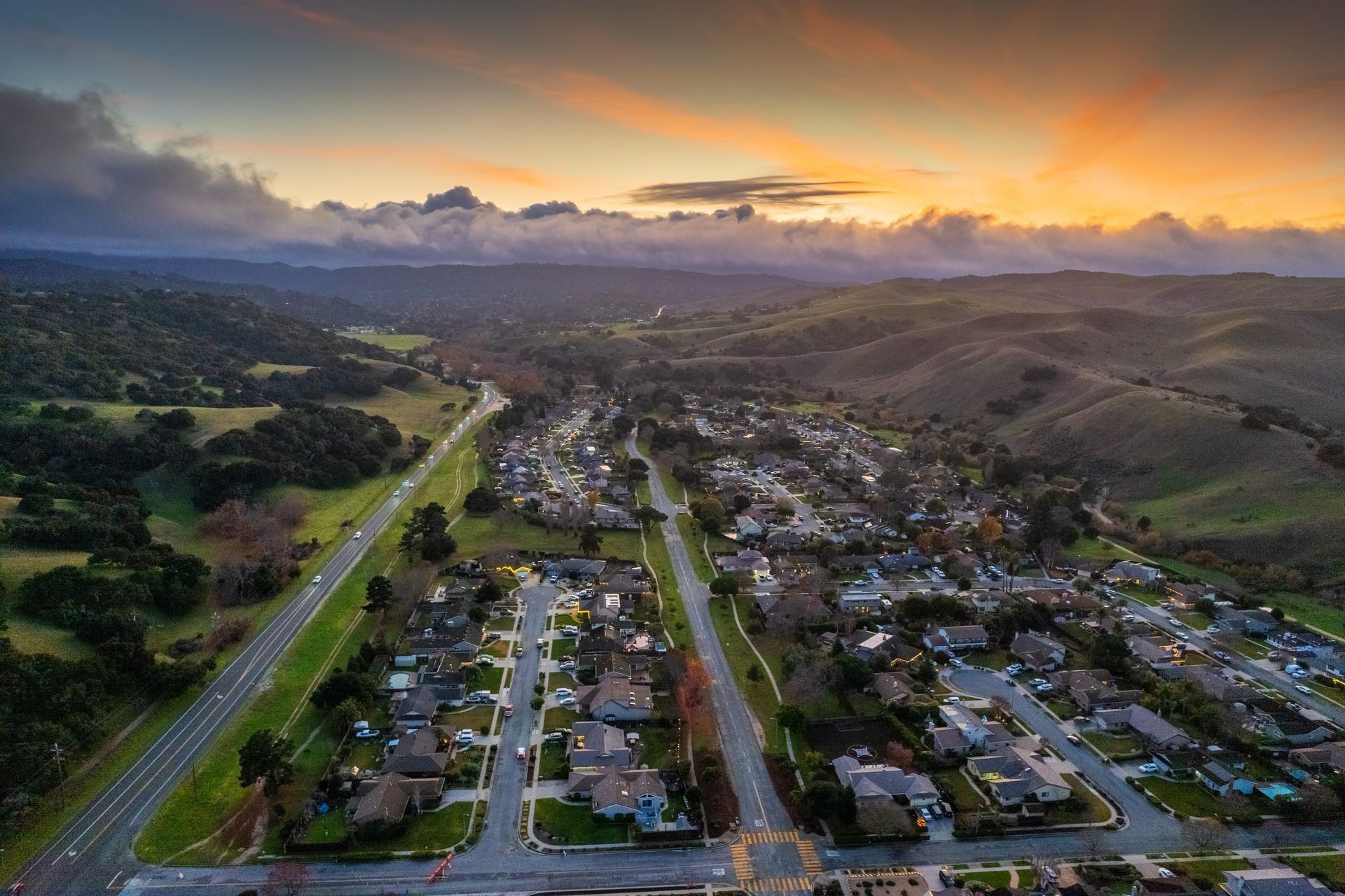 Aerial view of a suburban neighborhood at sunset with a highway on the left and hills in the background. Aerial view of a suburban neighborhood at sunset with a highway on the left and hills in the background.