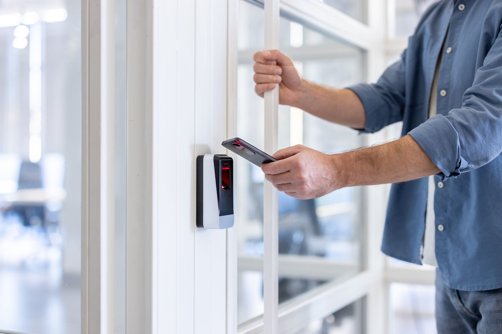 Man unlocking a glass door with a smartphone near a mounted access control device. Man unlocking a glass door with a smartphone near a mounted access control device.