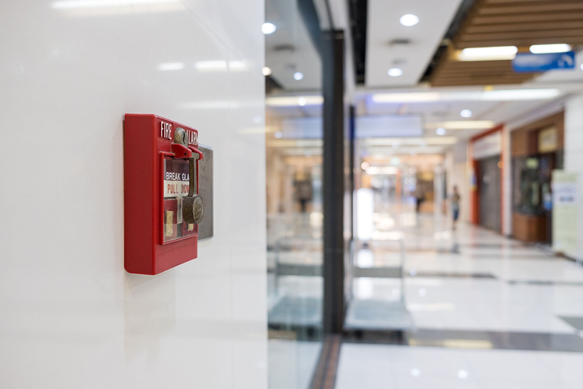 Red fire alarm box mounted on a white wall in a shopping mall hallway. Red fire alarm box mounted on a white wall in a shopping mall hallway.