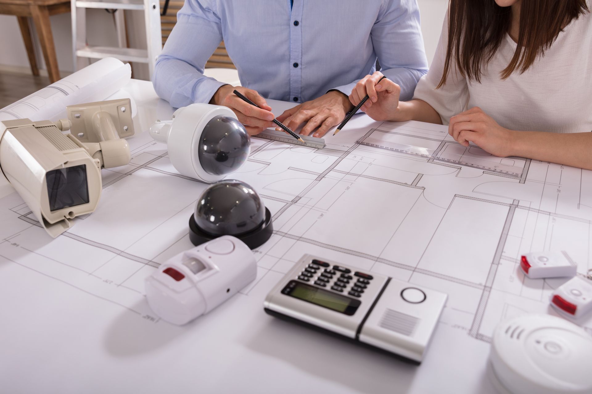 People planning a security system with blueprints, cameras, and sensors on a table.