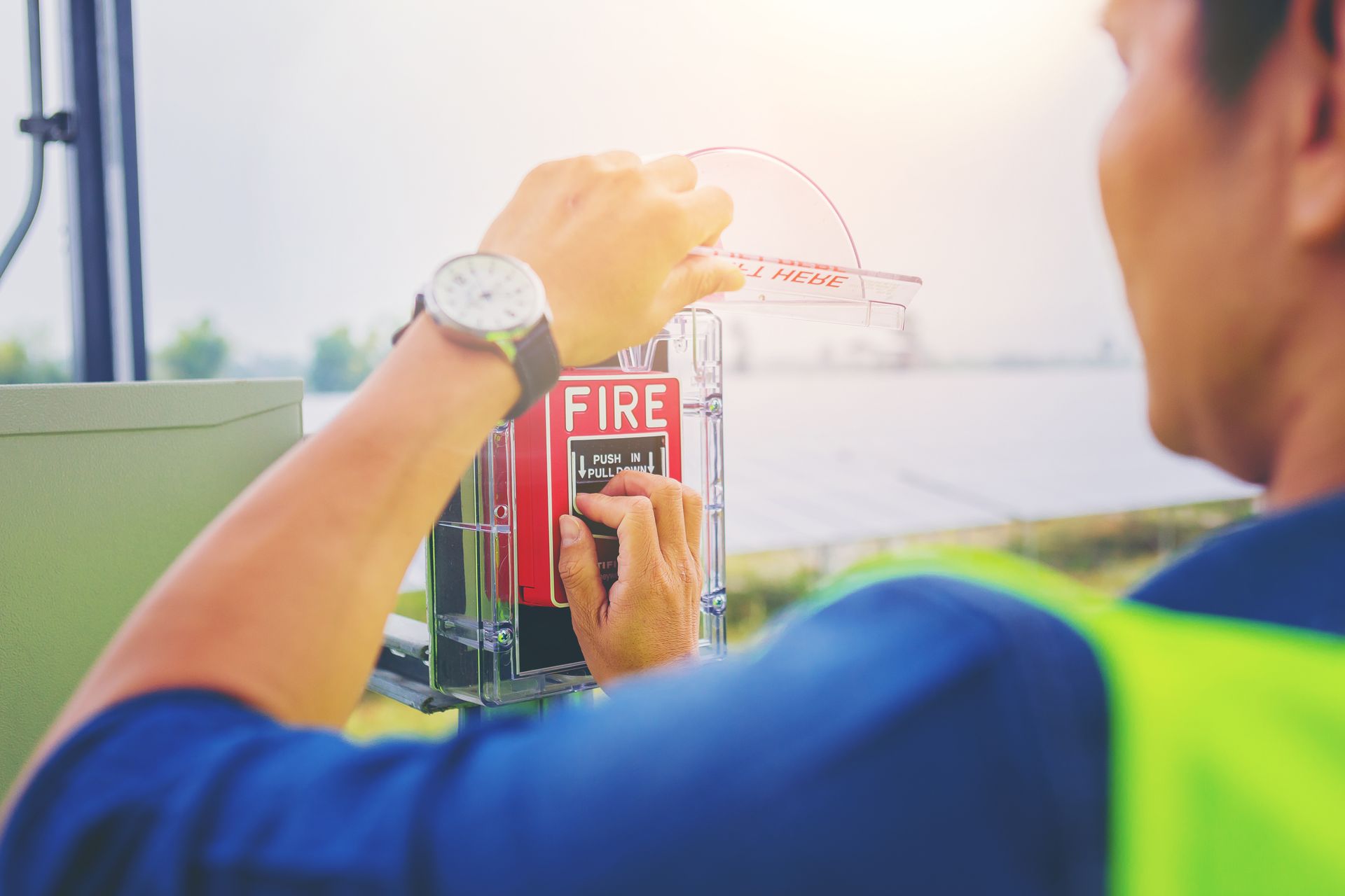 Person pulling a fire alarm lever outdoors. Red alarm box, fluorescent vest, watch. Person pulling a fire alarm lever outdoors. Red alarm box, fluorescent vest, watch.