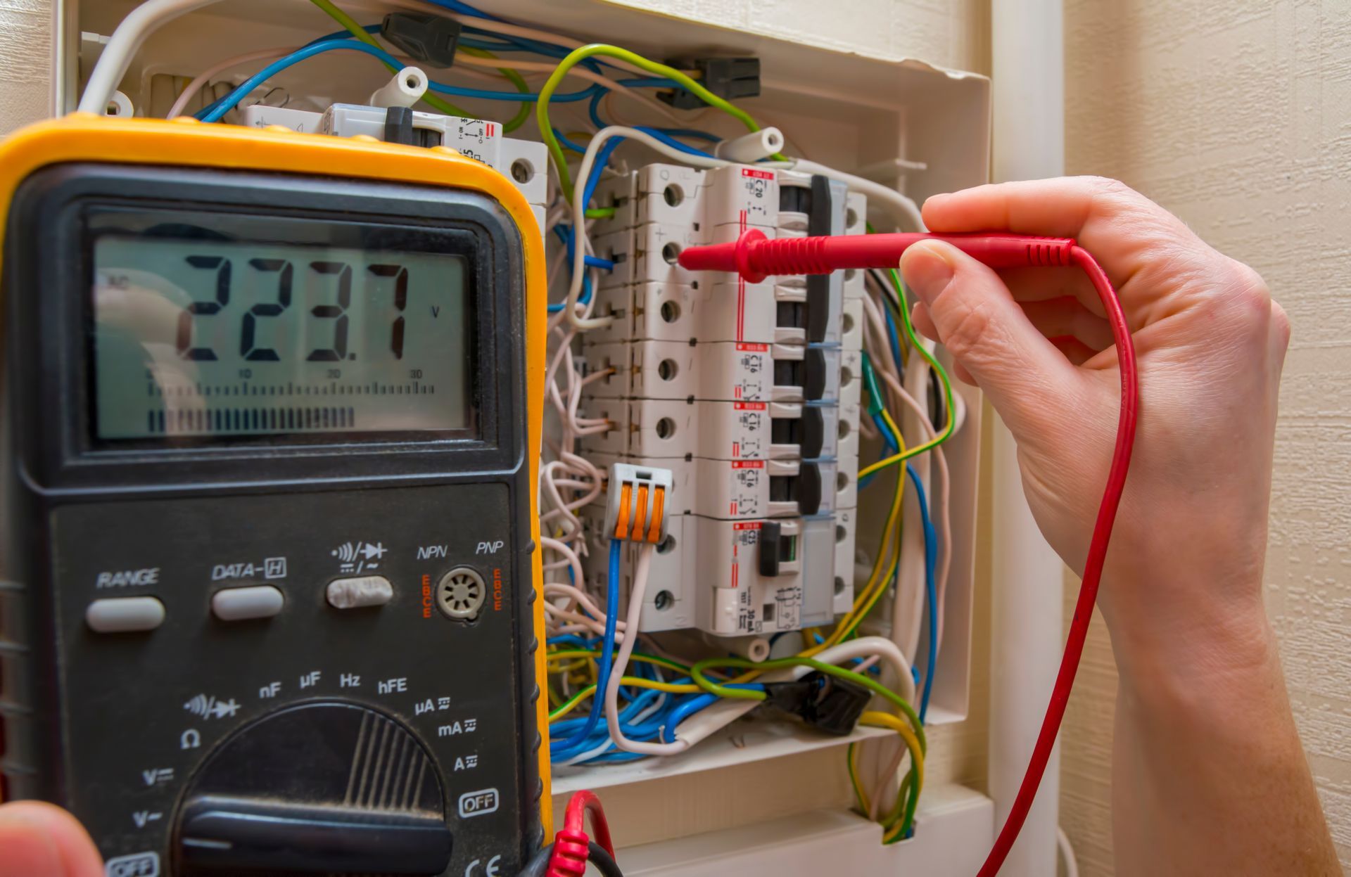 Person using a multimeter to test electrical panel; digital display reads 223.7.