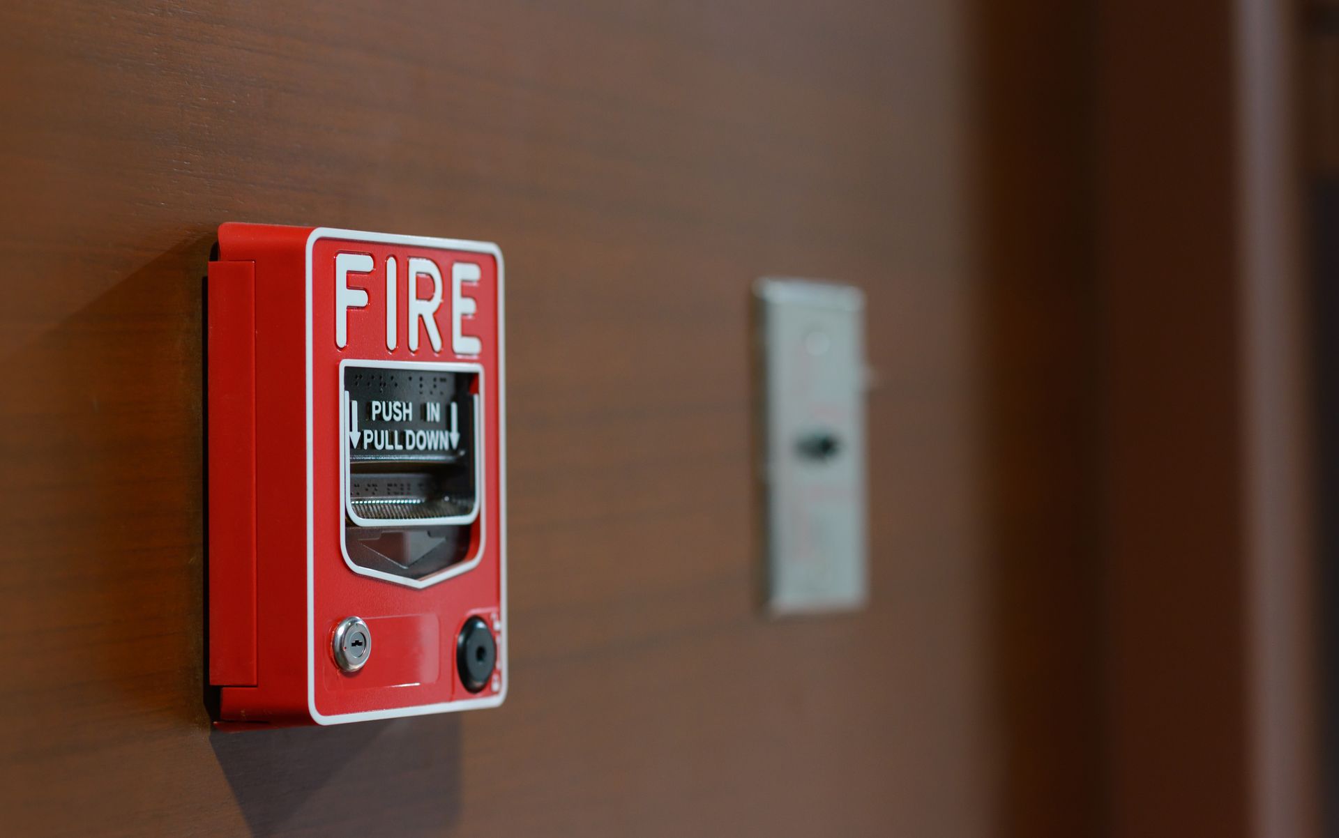 Red fire alarm box mounted on a brown wall, beside a white switch. Red fire alarm box mounted on a brown wall, beside a white switch.