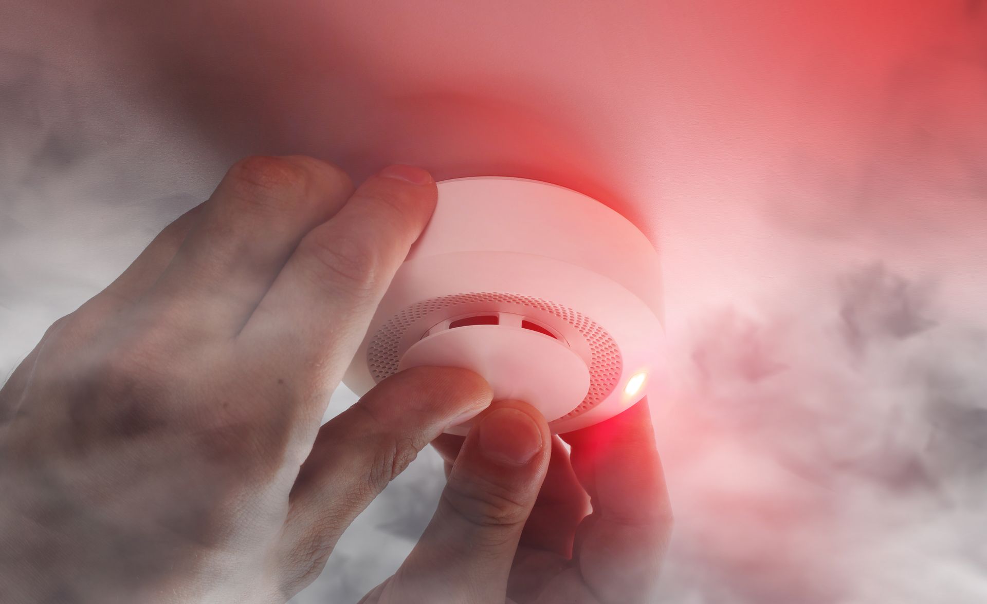 Hands reaching for a smoke detector, surrounded by smoke; red light flashing. Hands reaching for a smoke detector, surrounded by smoke; red light flashing.