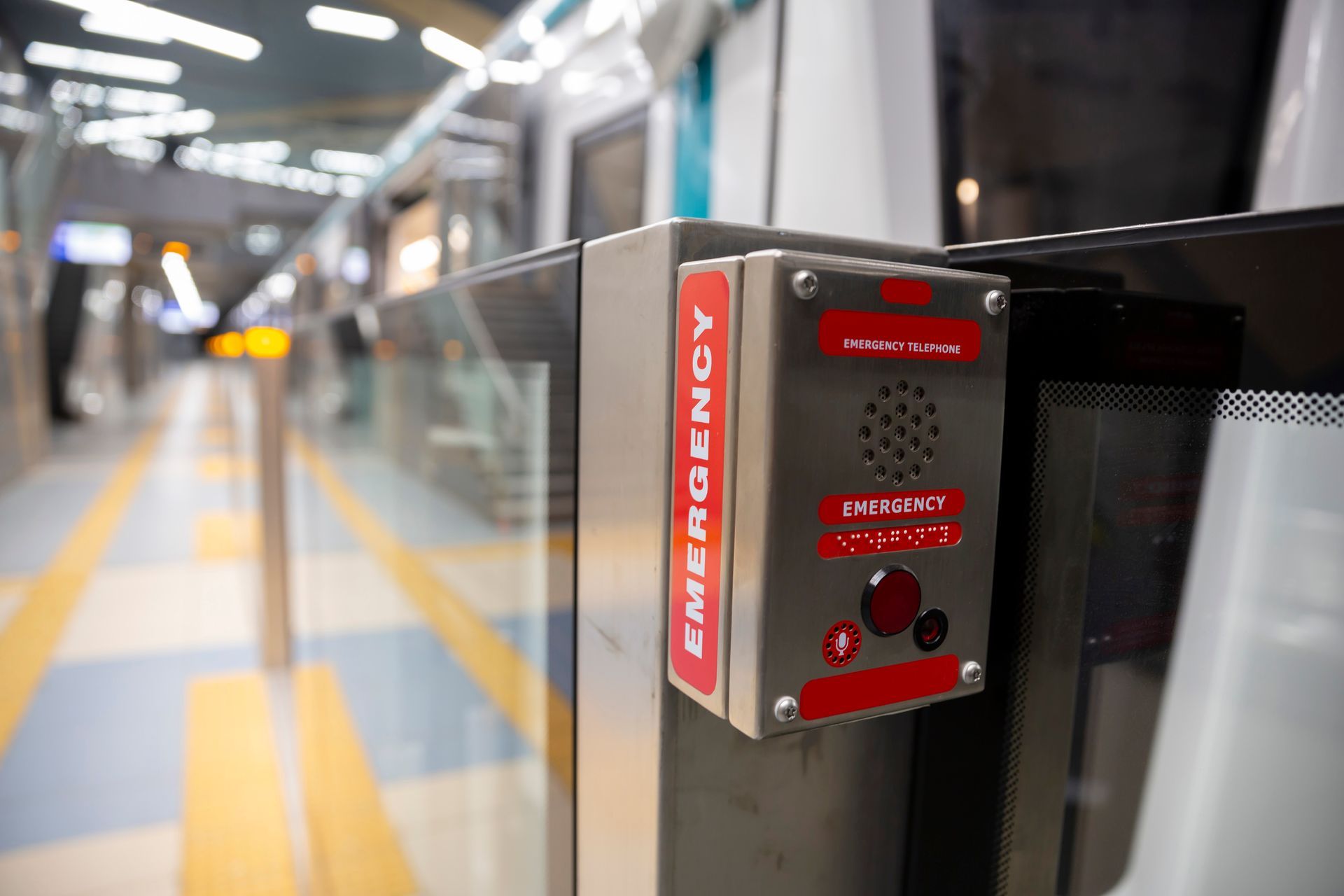 Emergency call button on a train platform. Red box with button and speaker next to glass door.