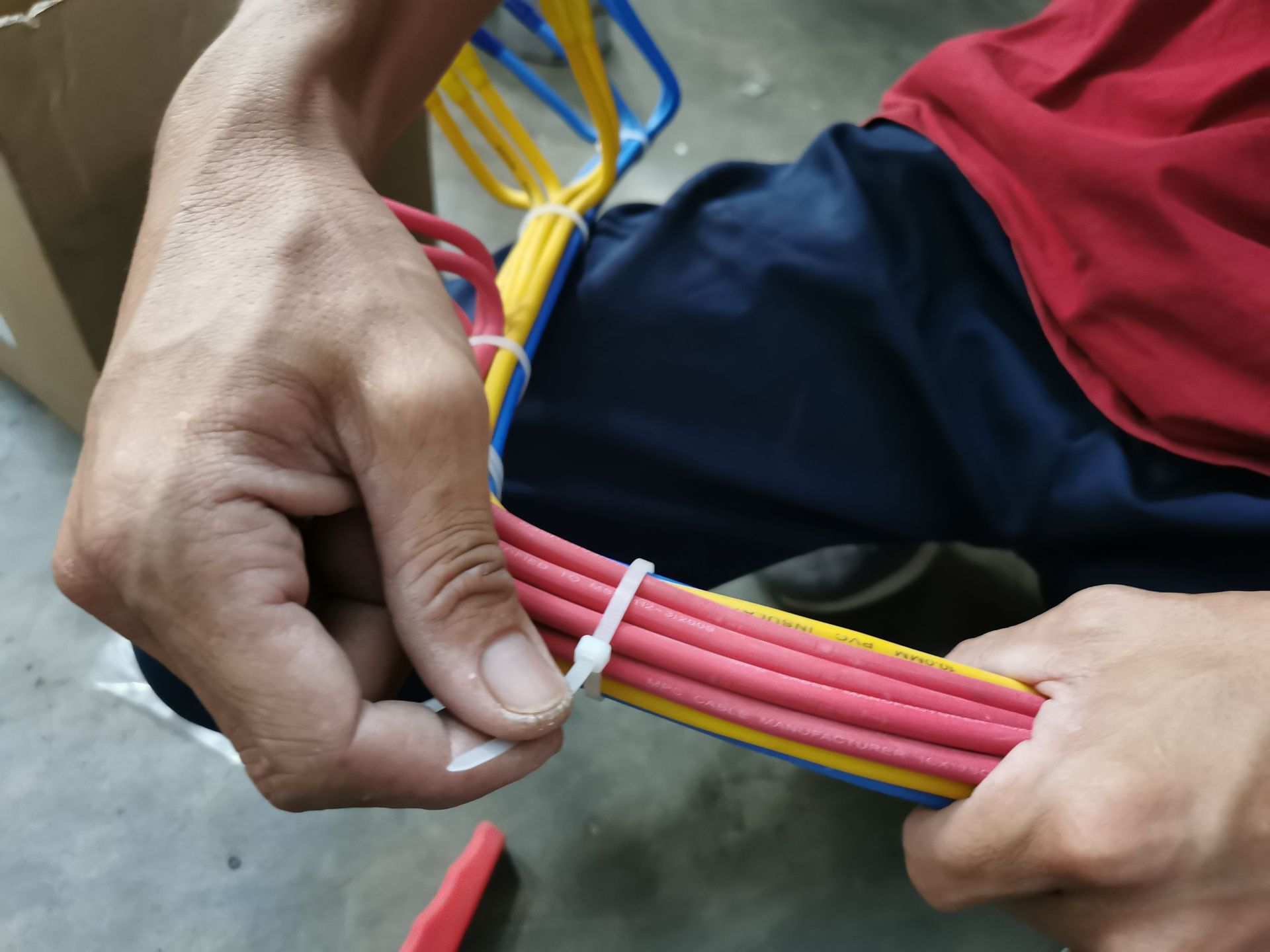 Person securing colored electrical wires with a white zip tie.