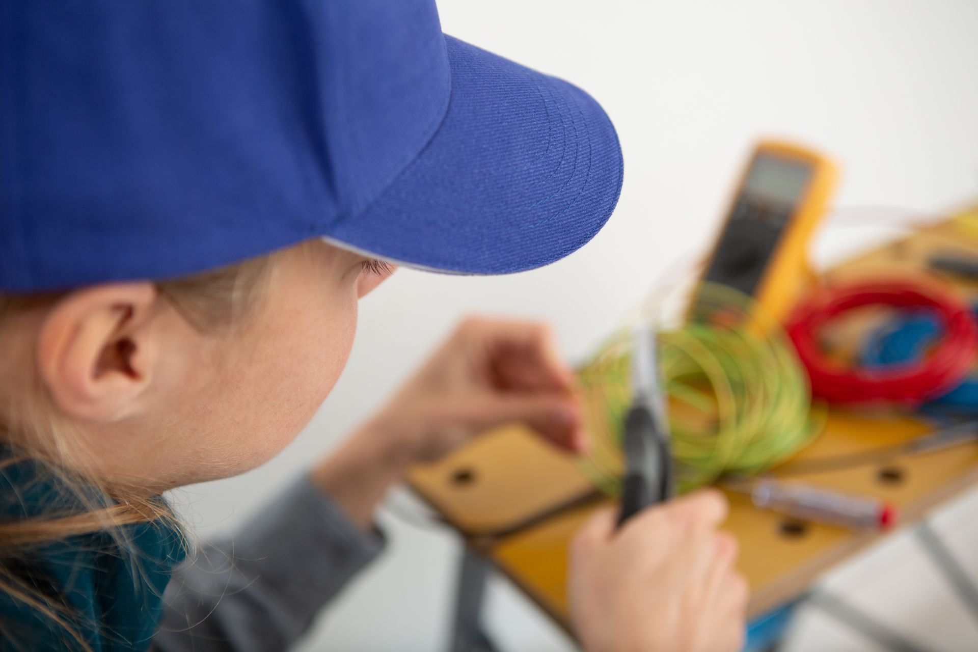 Person in blue cap working on electrical wiring with tools.