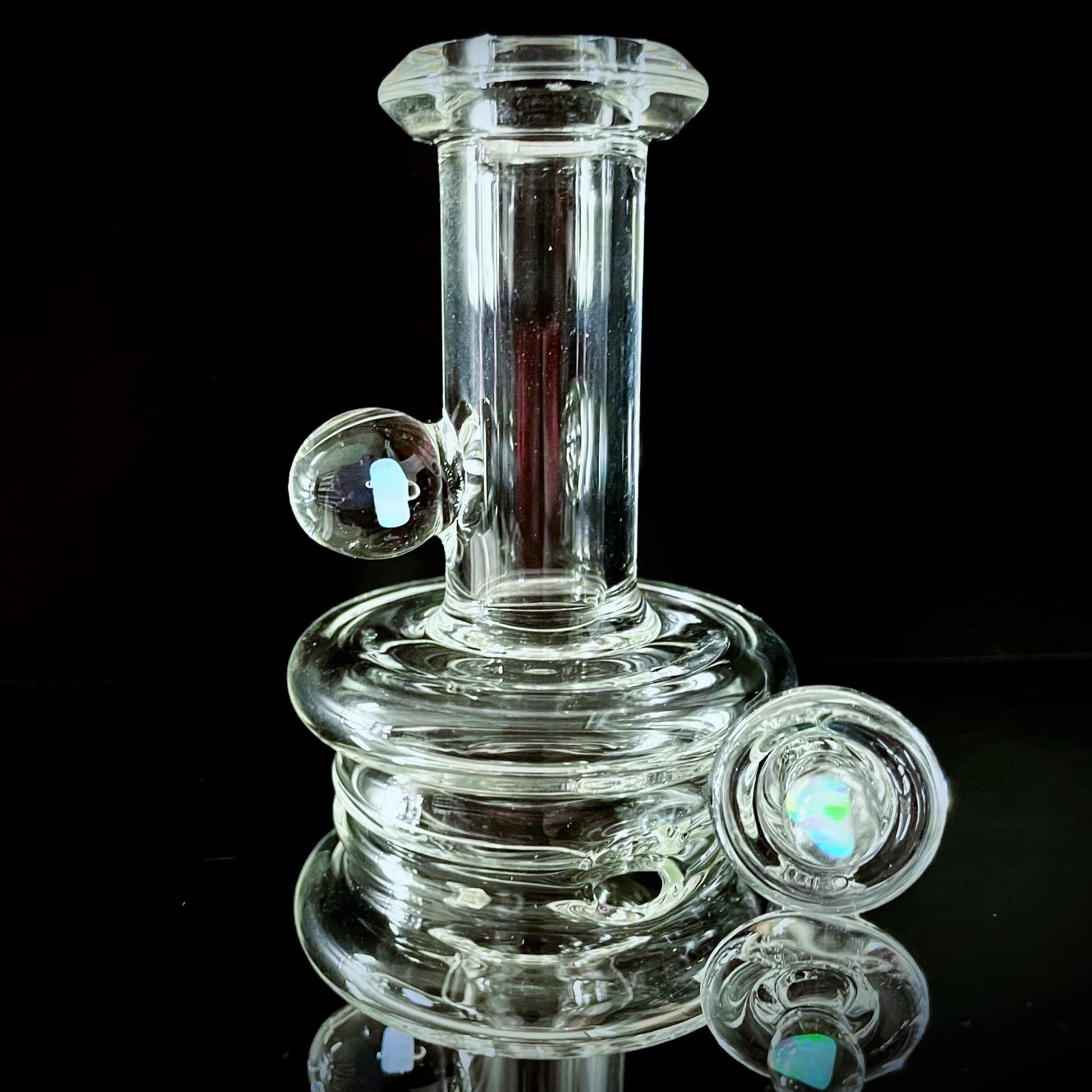 A clear glass bong is sitting on a black surface.