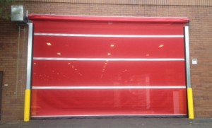 A red garage door is sitting on the side of a brick building.