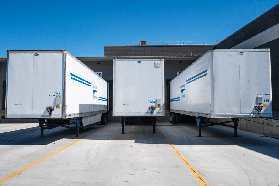A row of white semi trucks are parked in a parking lot.