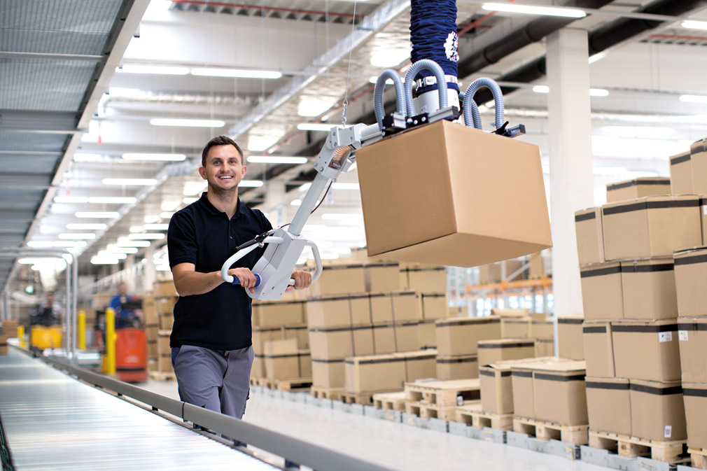 A man is carrying a cardboard box on a conveyor belt in a warehouse.