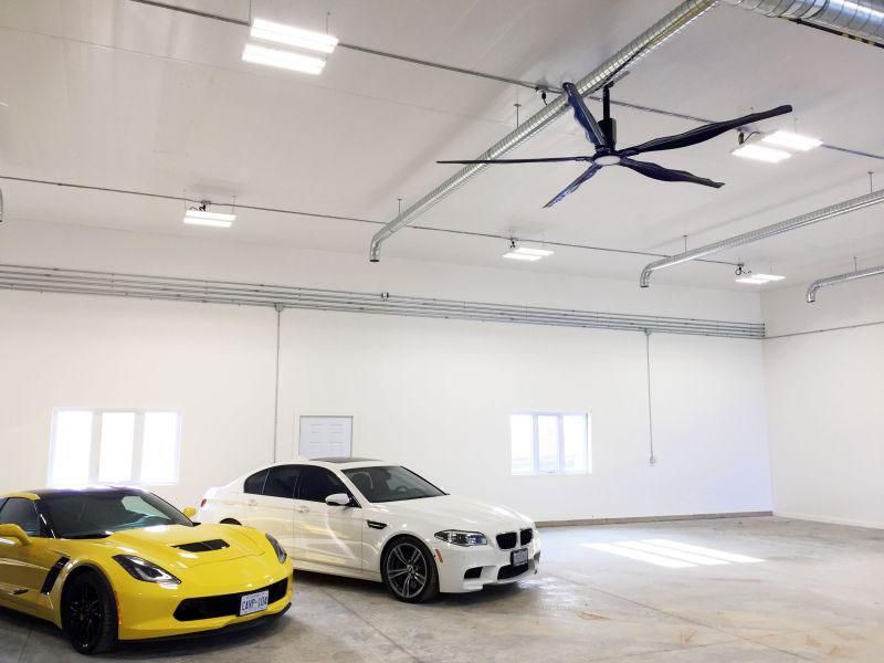 Two cars are parked in a garage with a ceiling fan.