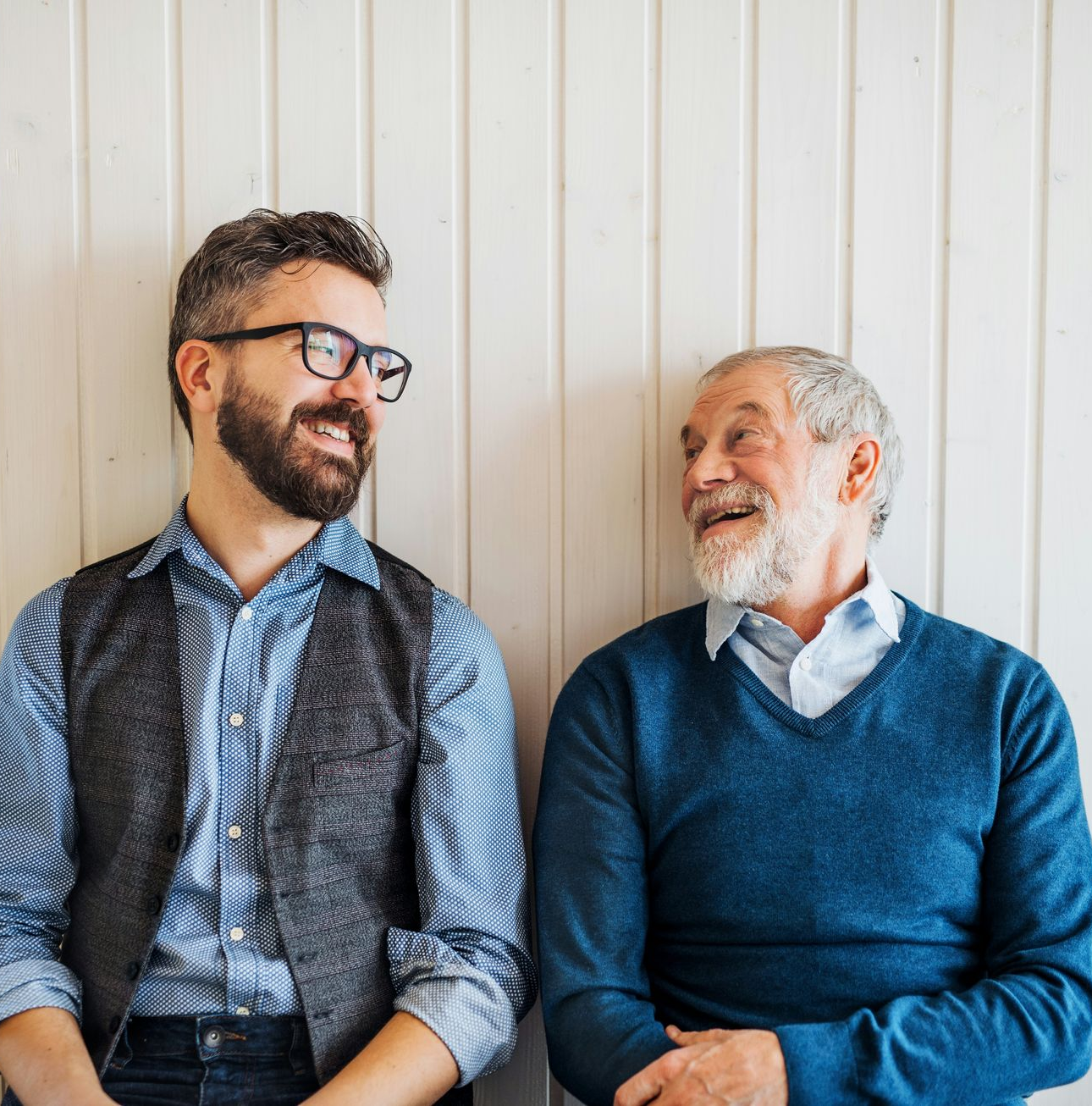 A man in a blue shirt and tie is smiling with his arms crossed