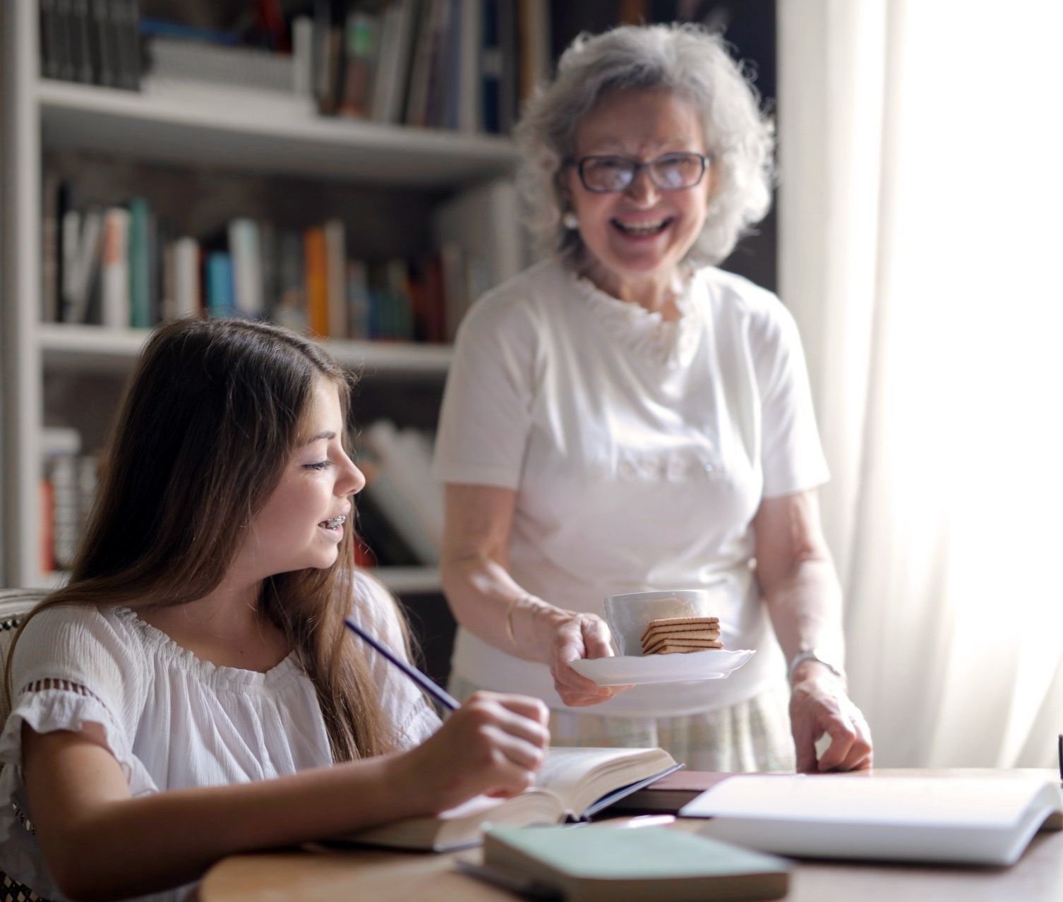 A young girl is sitting at a table with an older woman standing behind her.