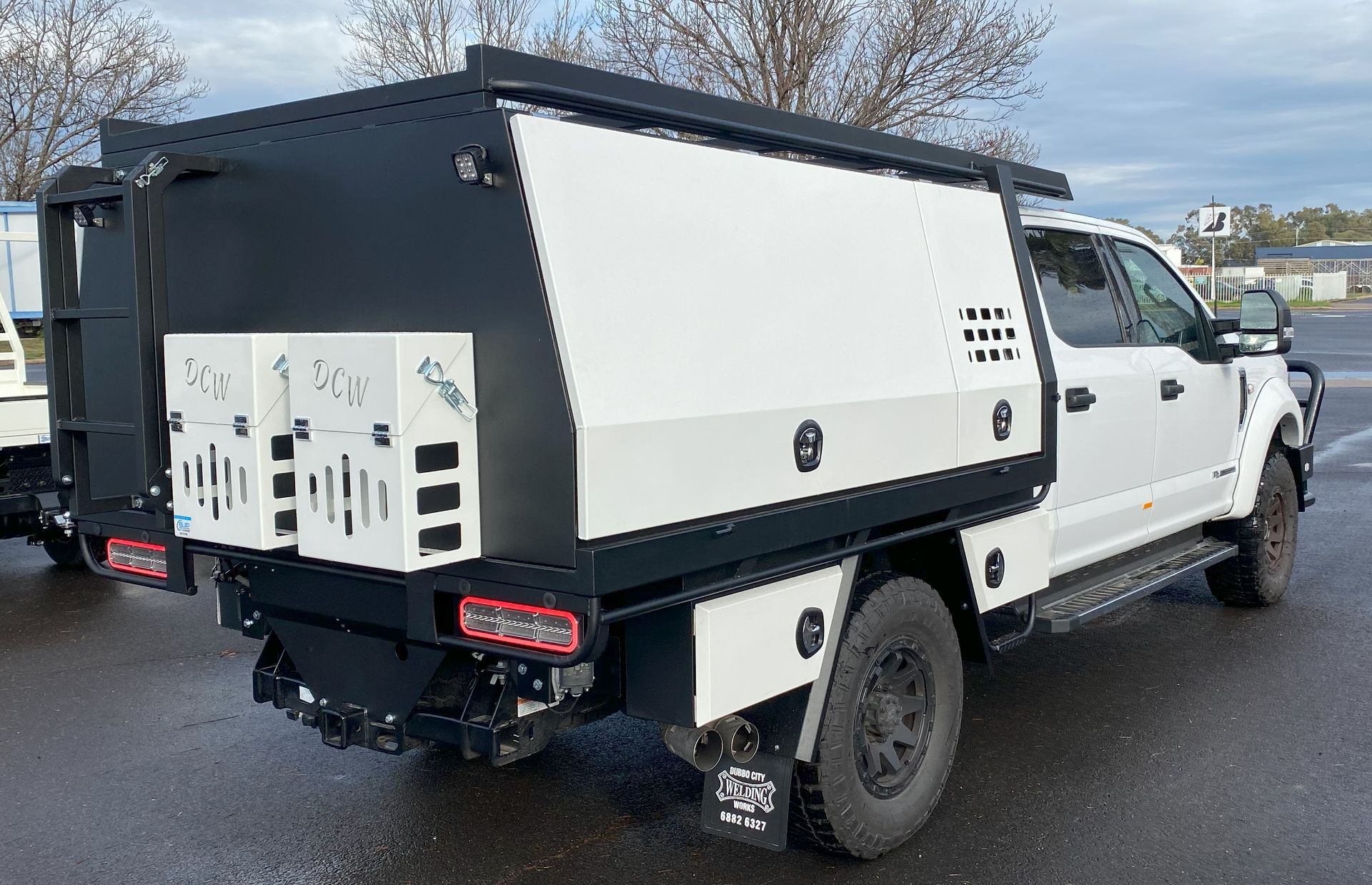 A white truck with a black canopy is parked in a parking lot.