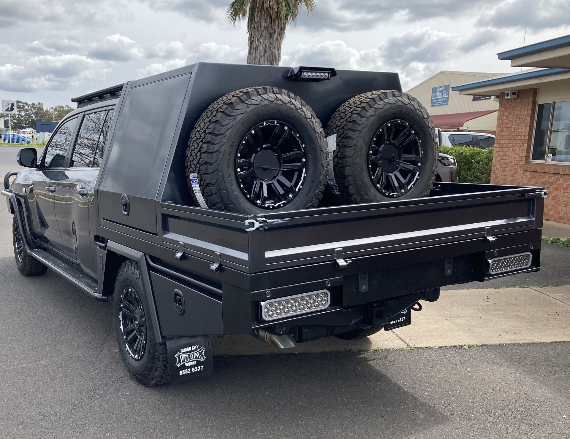 A black truck with two tires in the bed is parked on the side of the road.