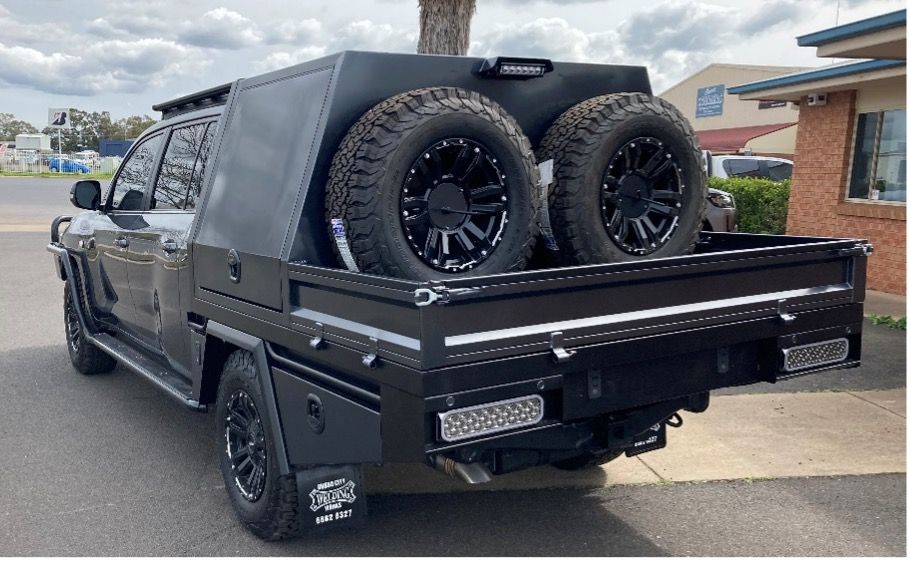 Black Pickup Truck With Custom Flatbed, Spare Tires, And Tool Box Parked Outdoors