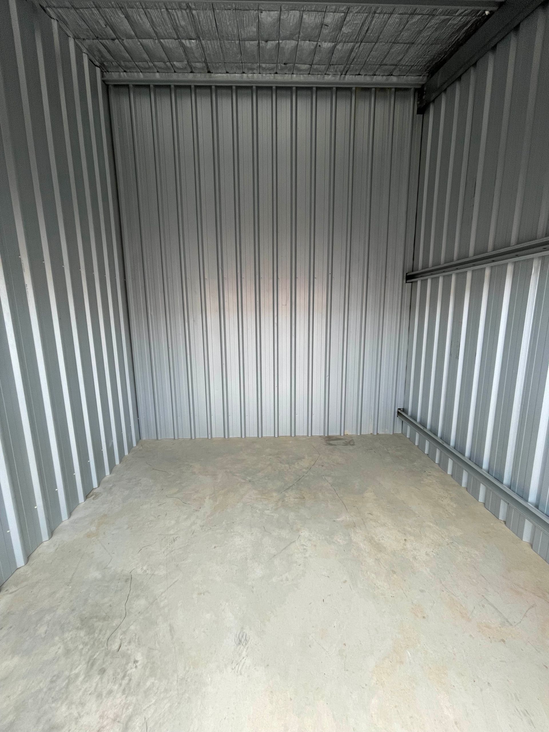 Empty corrugated metal storage unit with a concrete floor and bare walls