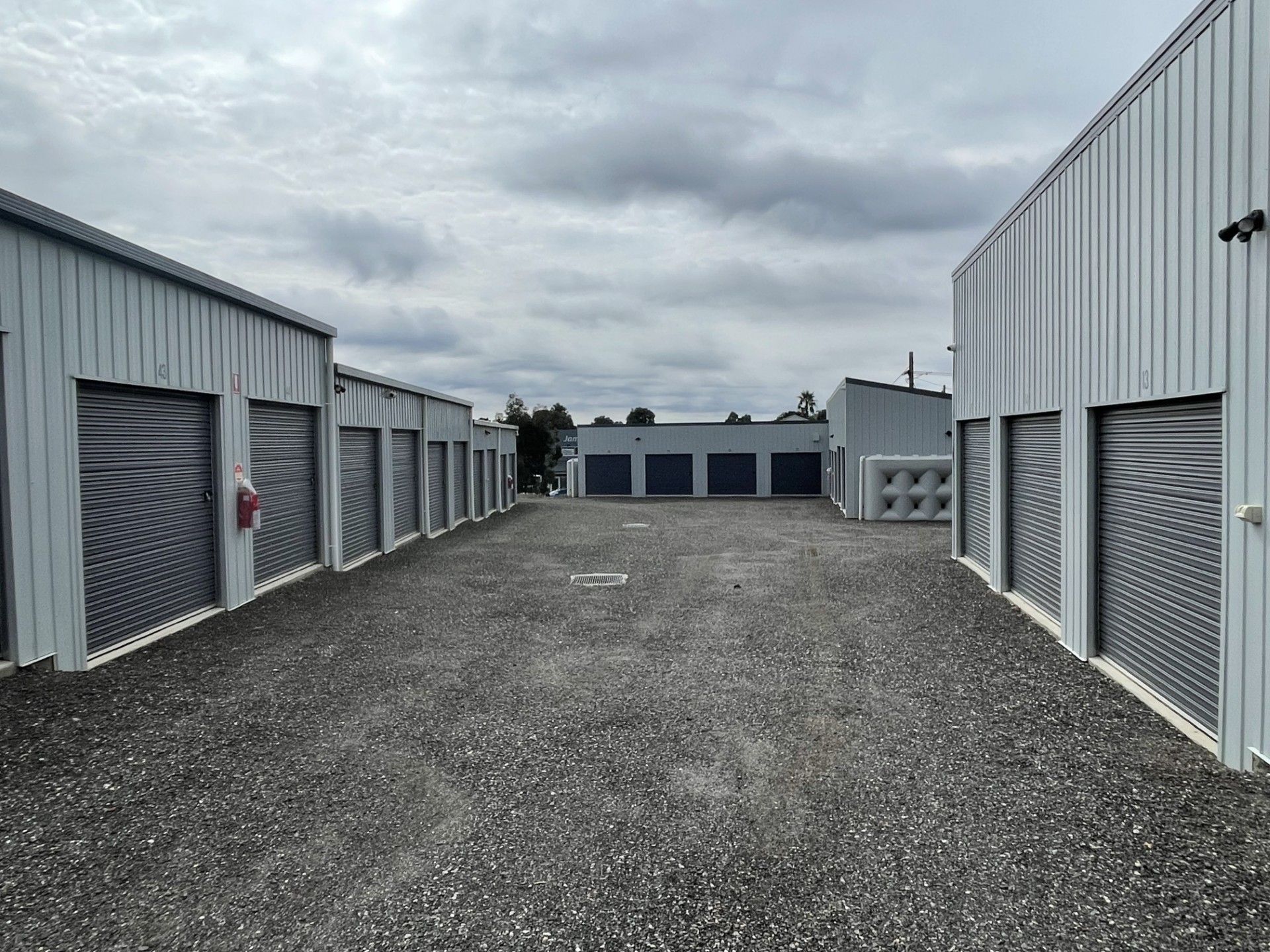 A gravel driveway lined with gray metal self-storage units under a cloudy sky.