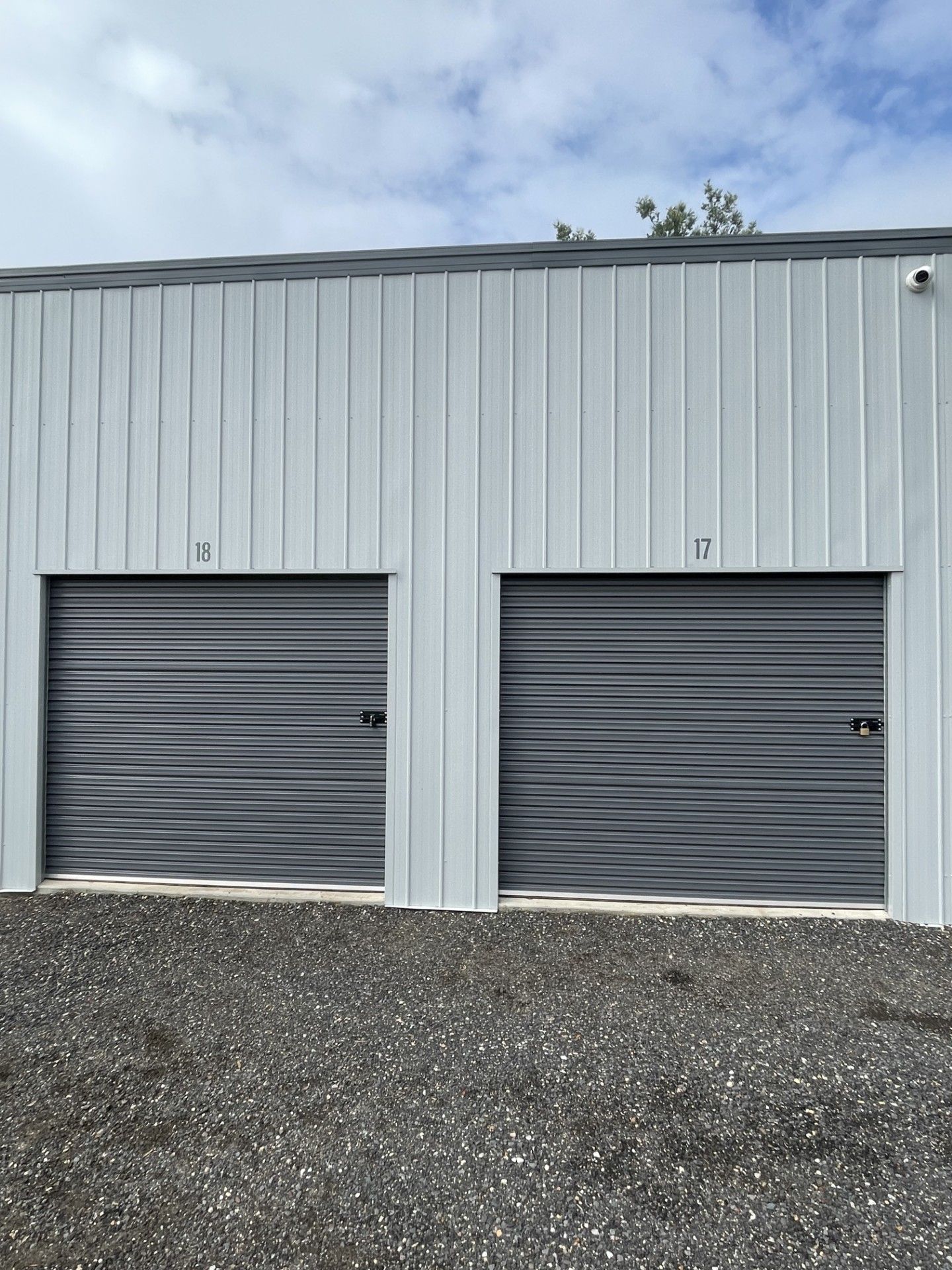 Two gray, corrugated metal storage unit doors, labeled 10 and 11, set in a light-colored building over gravel ground.