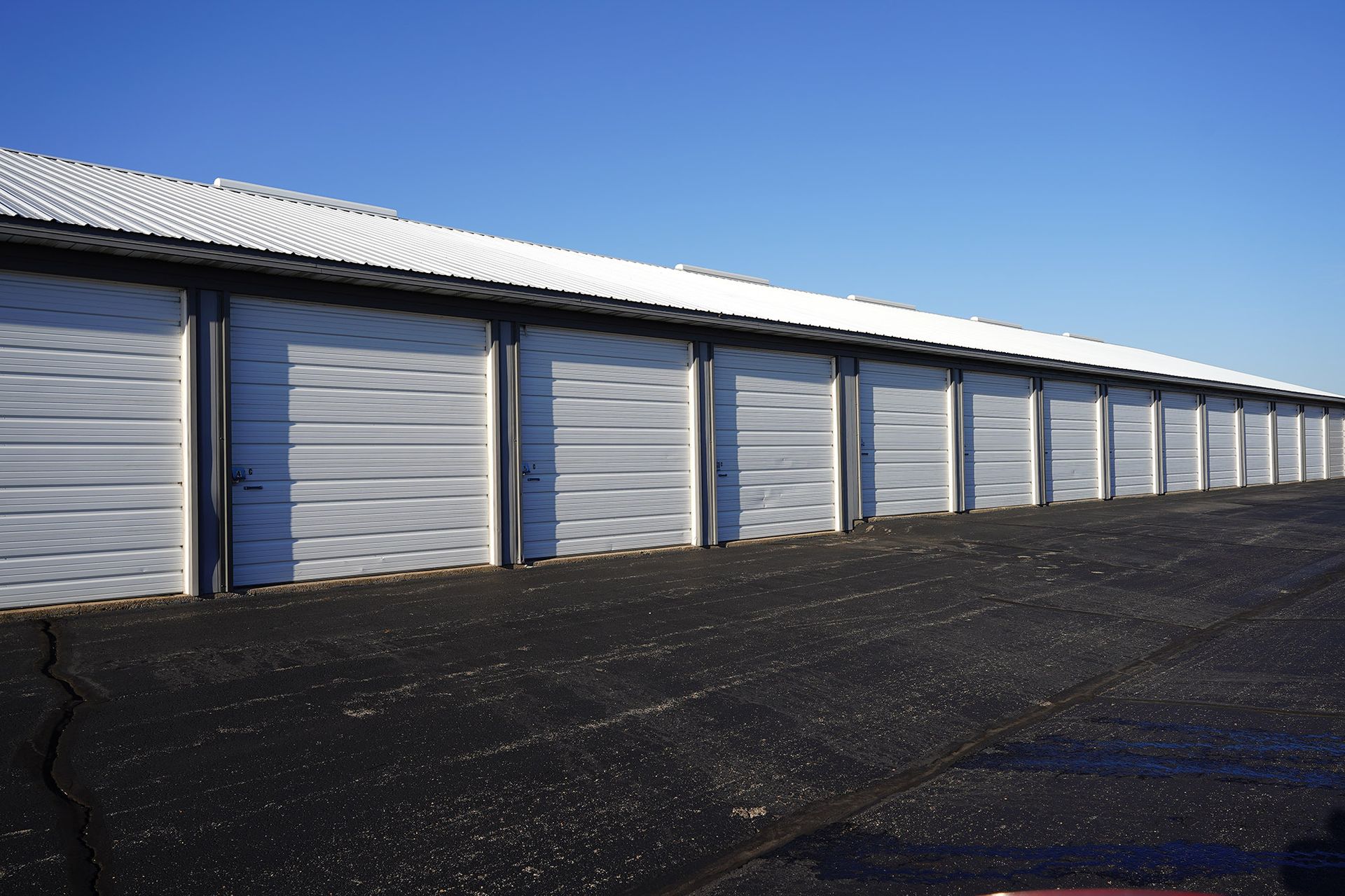 A long row of white metal self-storage unit doors under a clear blue sky, viewed from an angled perspective.