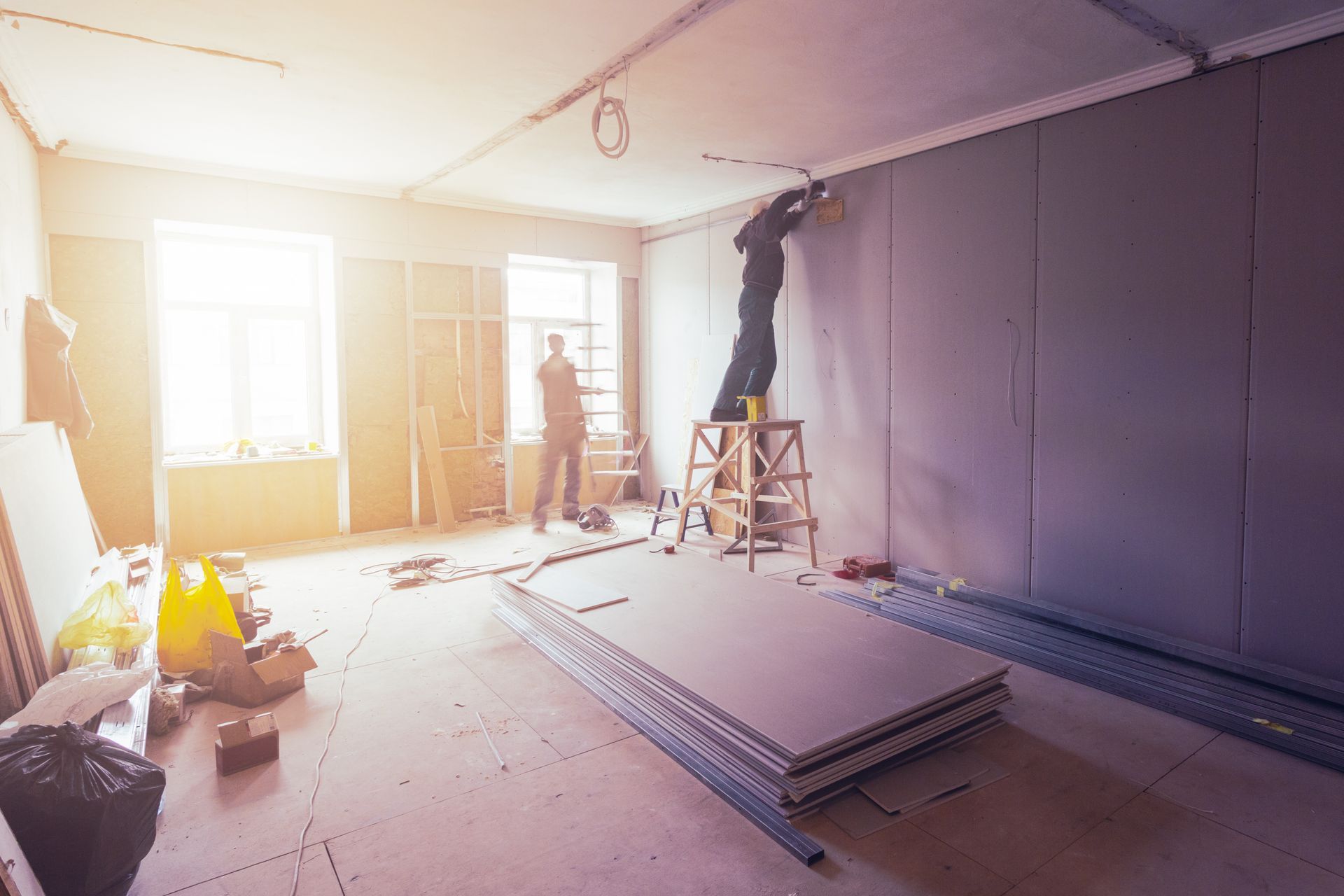 A man is standing on a ladder in a room under construction.