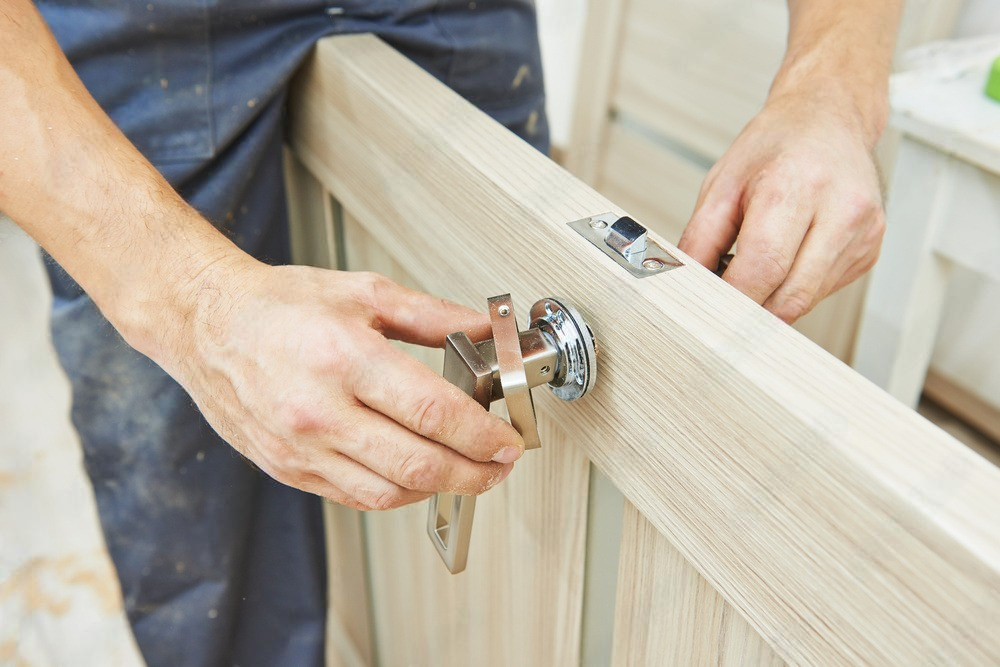 A man is installing a door handle on a wooden door.