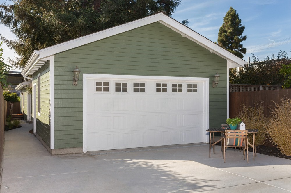 A green house with a white garage door and a table in front of it.