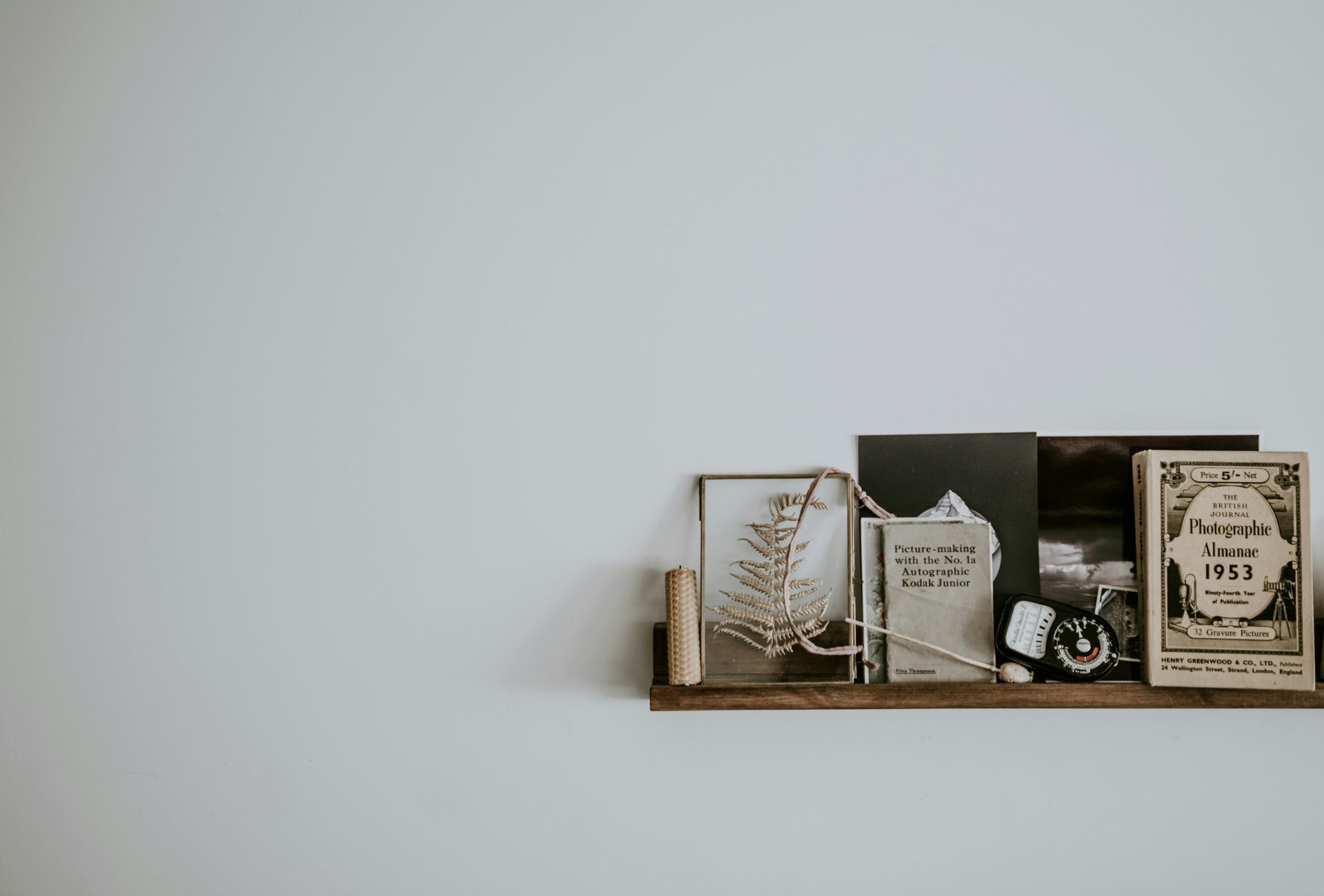 A wooden shelf filled with books and pictures on a white wall.