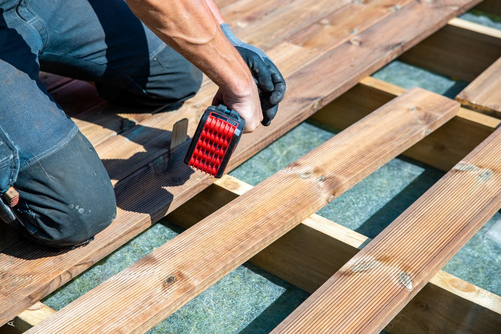 A man is working on a wooden deck with a drill.