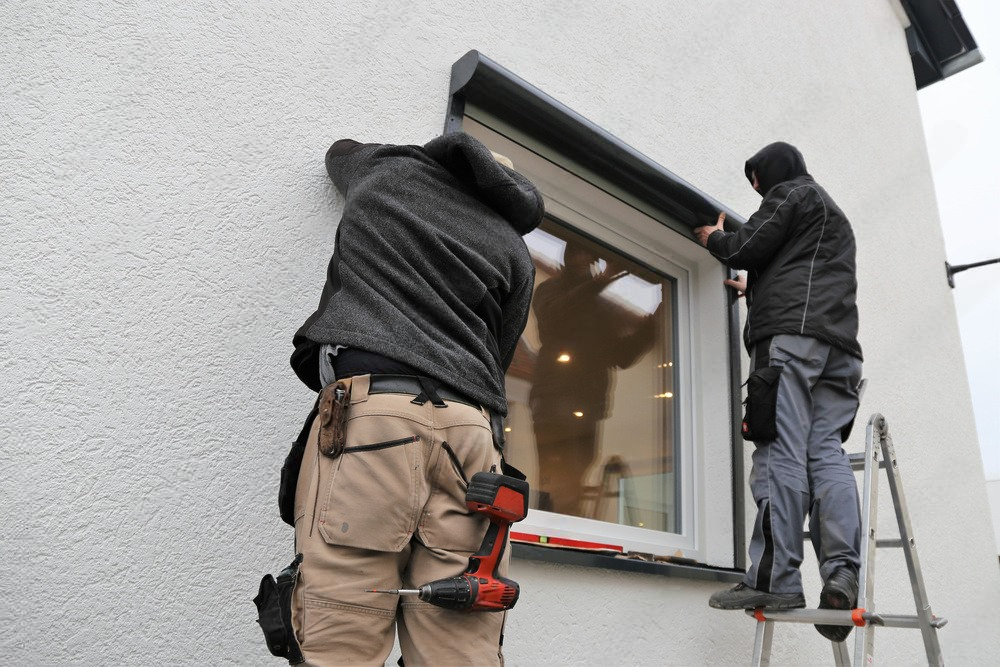 Two men are working on a window on the side of a building.