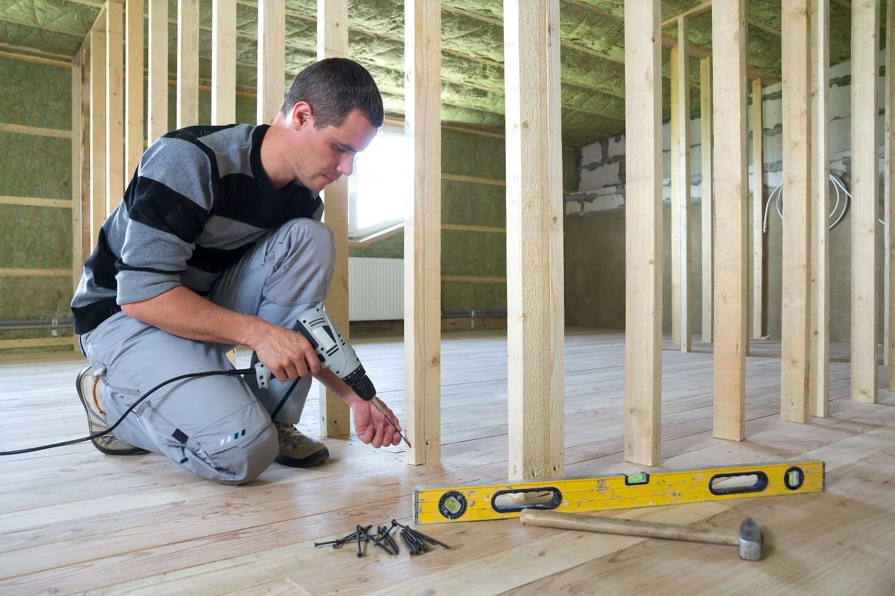 A man is working on a wooden floor with a drill and a level.