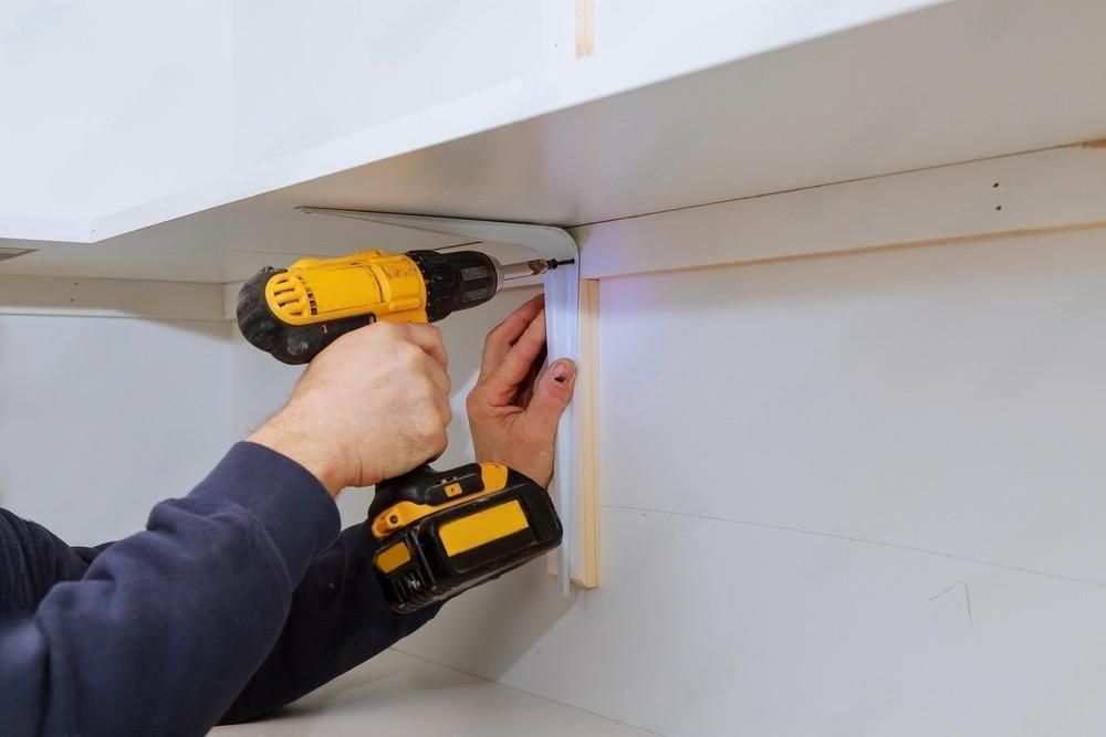 A man is using a drill to install a shelf in a kitchen.