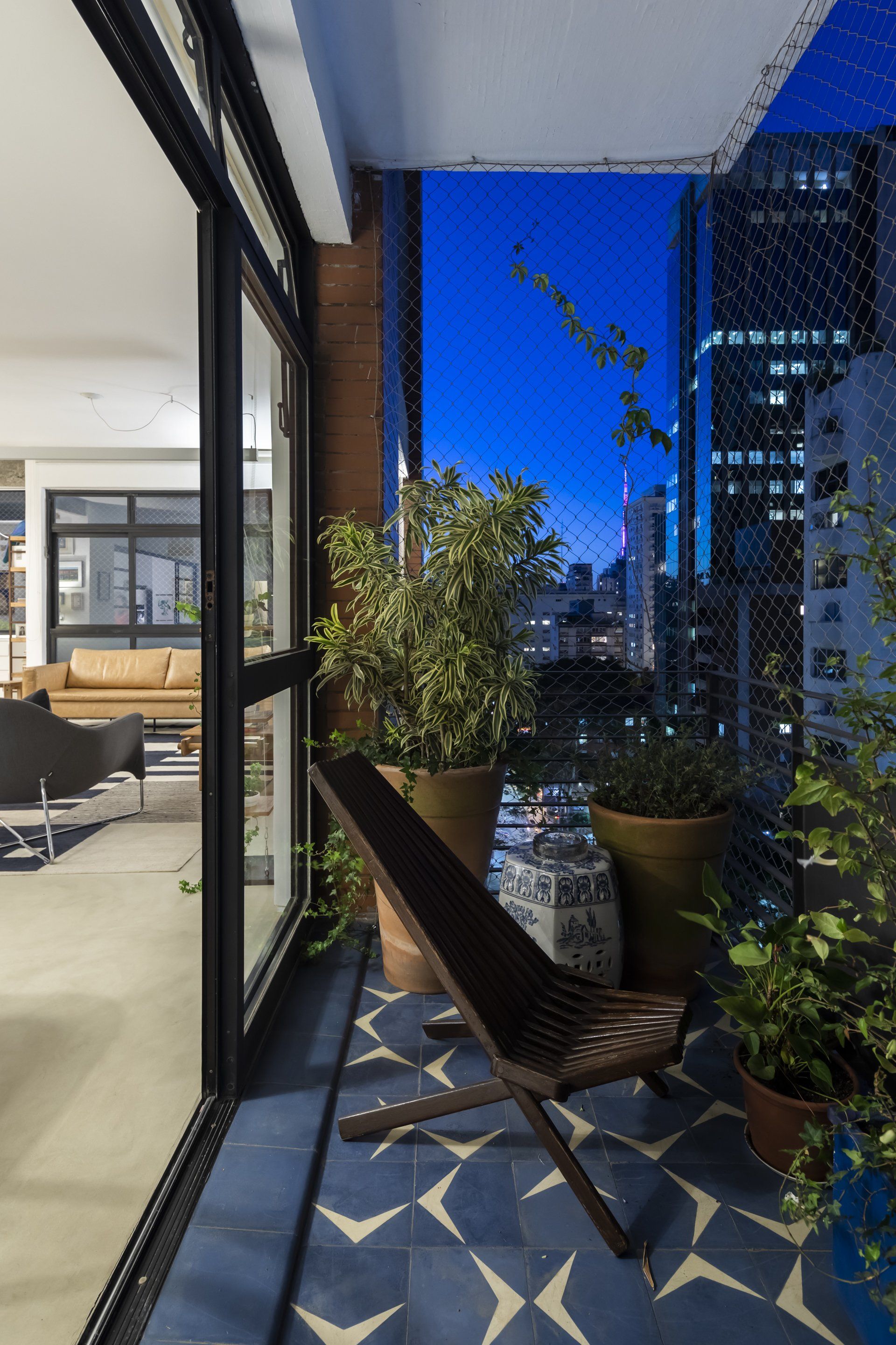 Uma varanda com cadeira e vasos de plantas e vista para a cidade à noite.