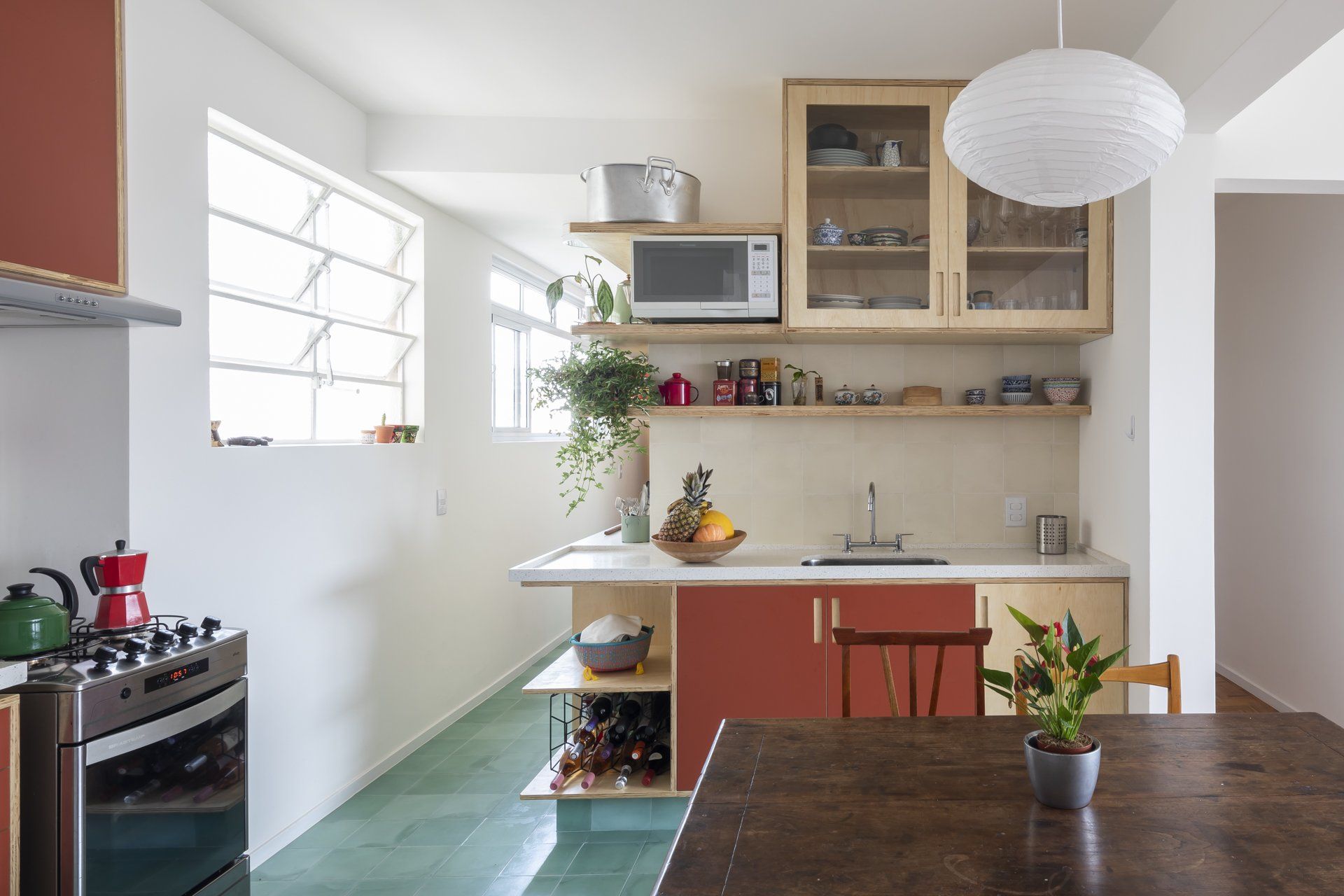 Uma cozinha com armários vermelhos, fogão, micro-ondas, pia e mesa.