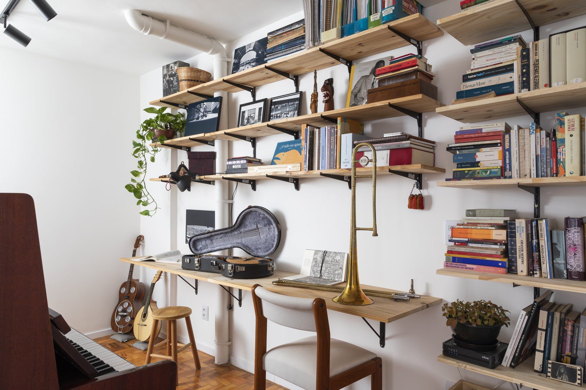 Uma sala com piano, escrivaninha, estantes e trombone.