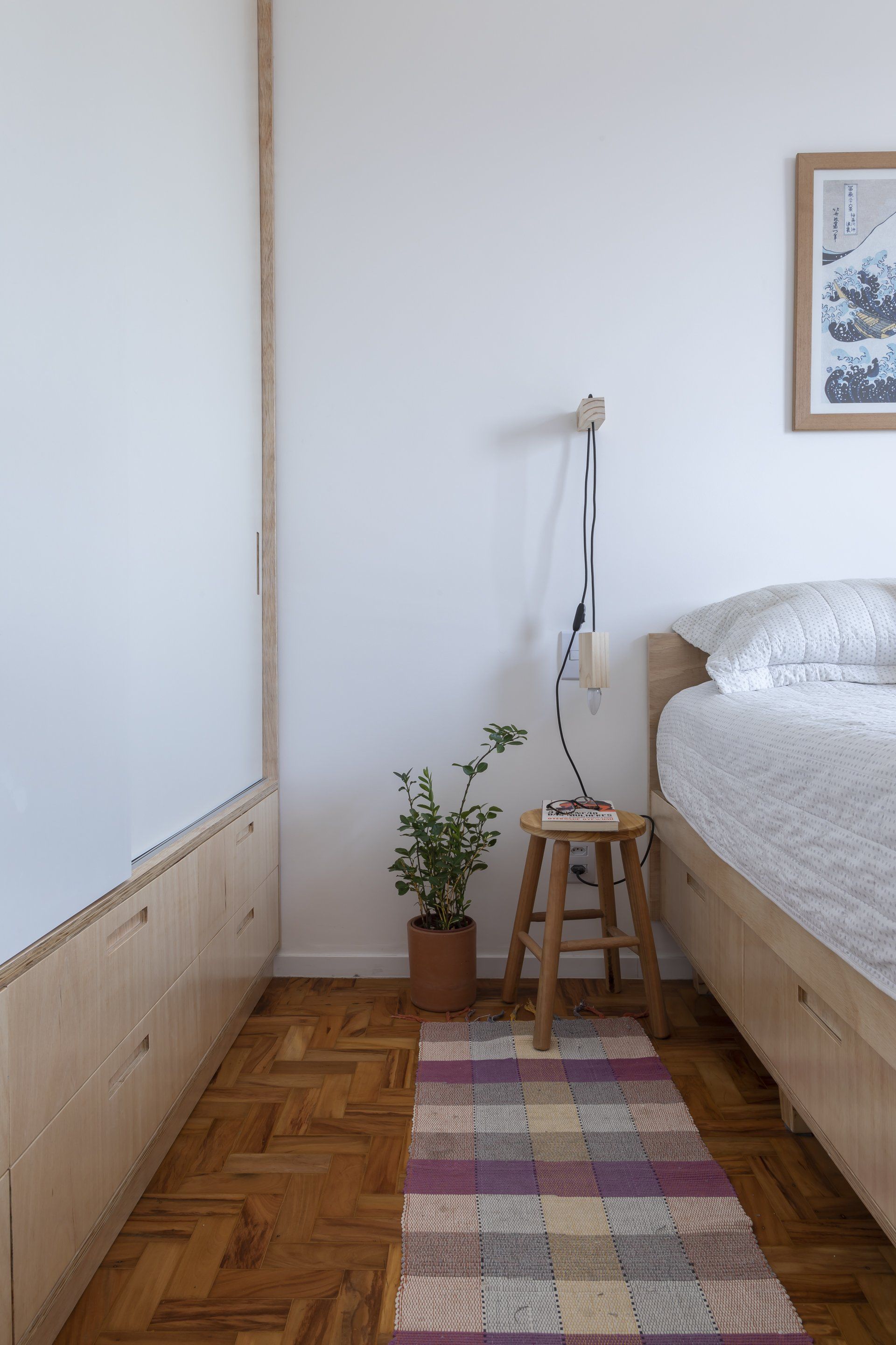 Um quarto com cama, banco, planta e tapete.