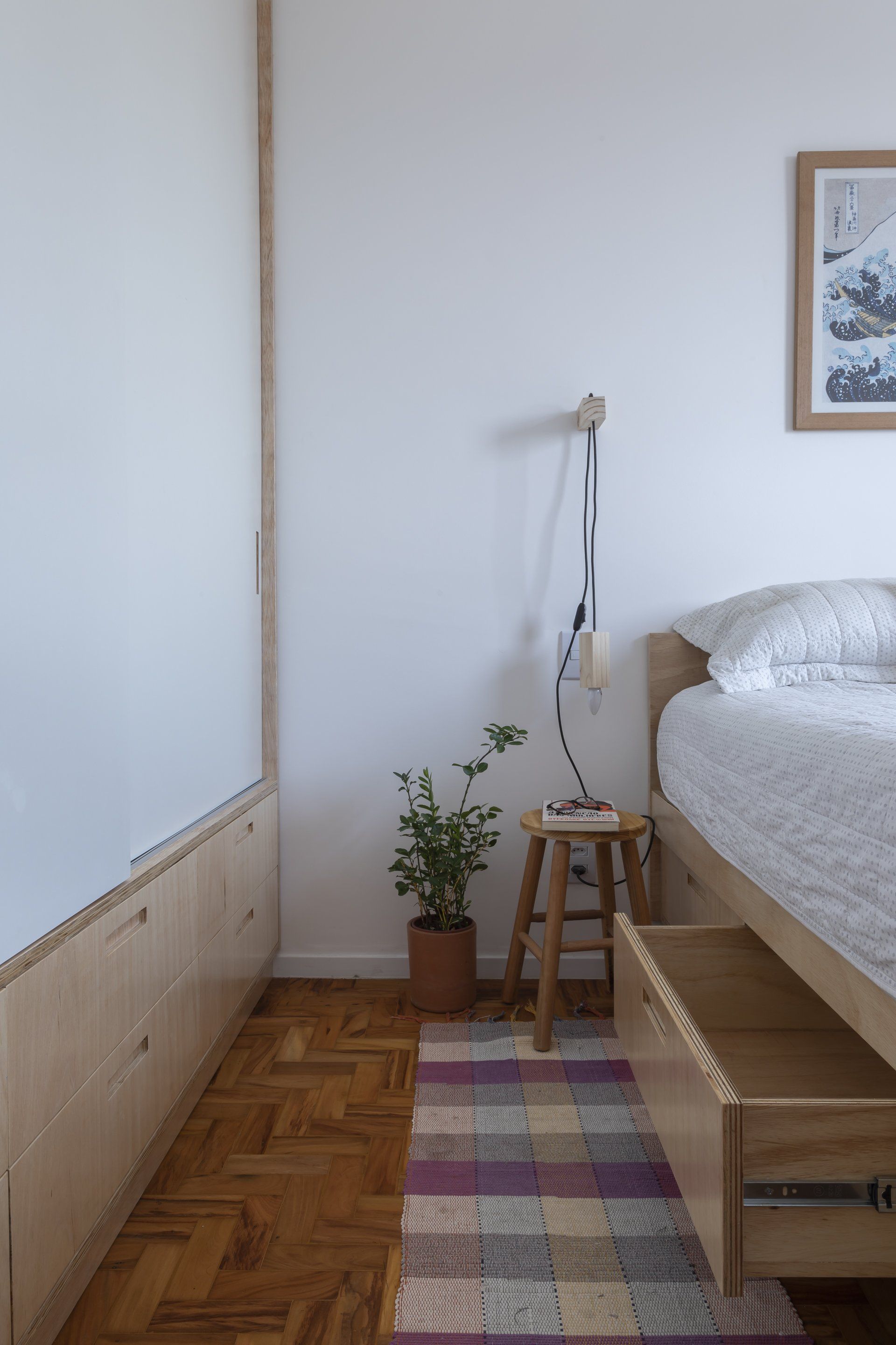 Um quarto com cama, banquinho, tapete e gavetas embaixo da cama.