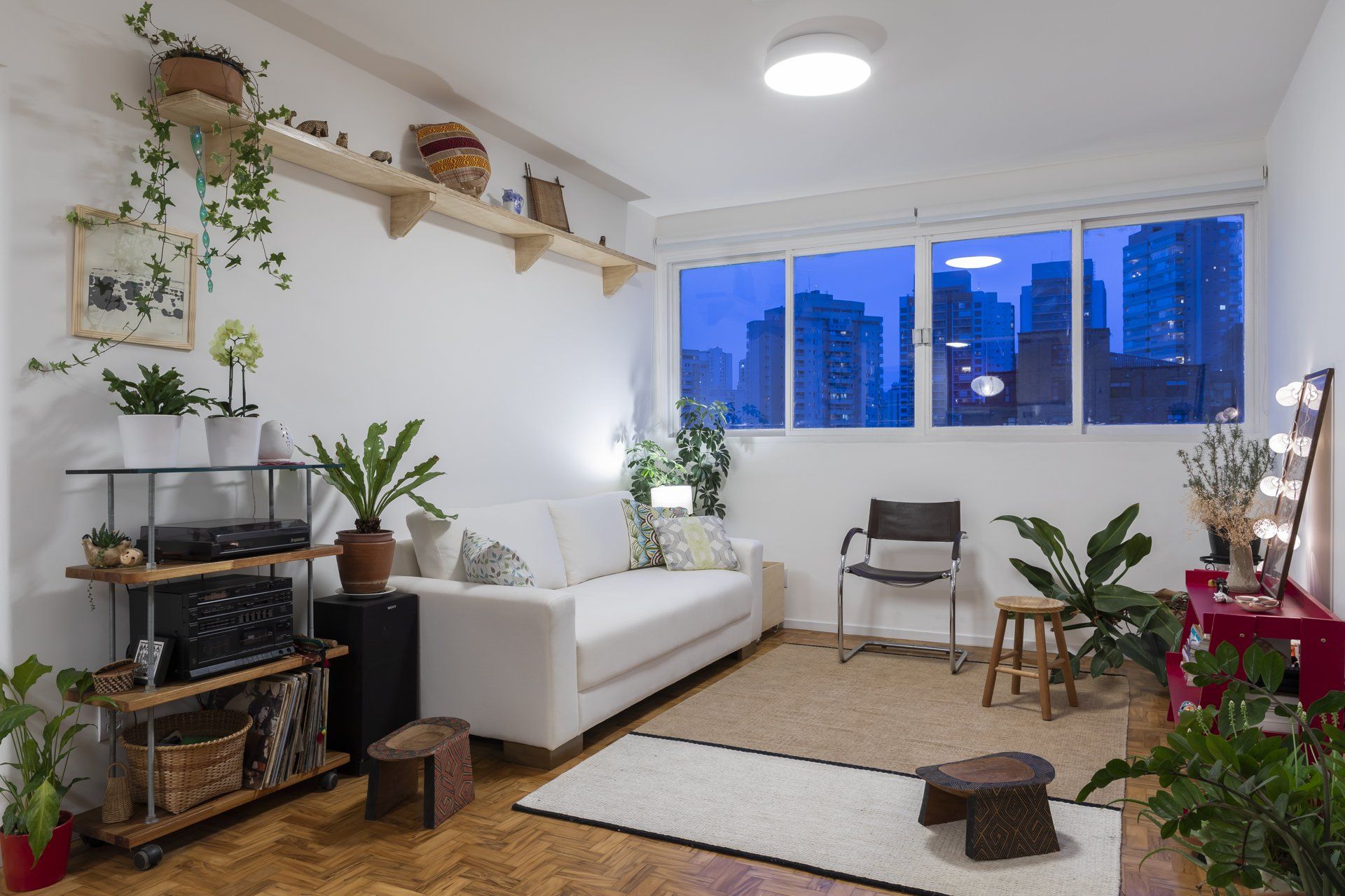 Uma sala com sofá, cadeiras, plantas e uma grande janela.