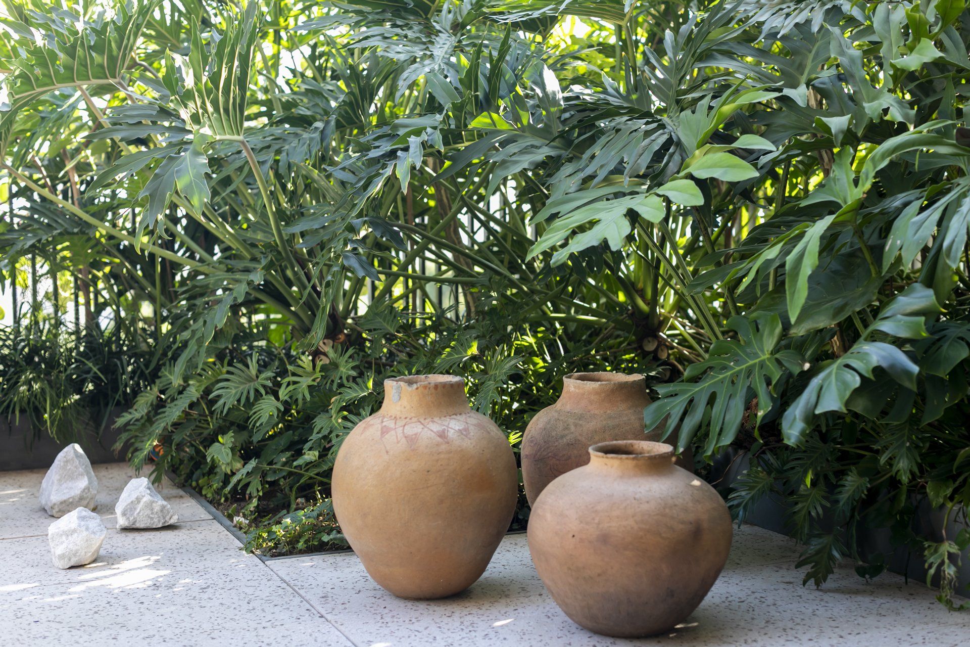 Três potes de barro estão em um pátio em frente a um jardim verdejante.