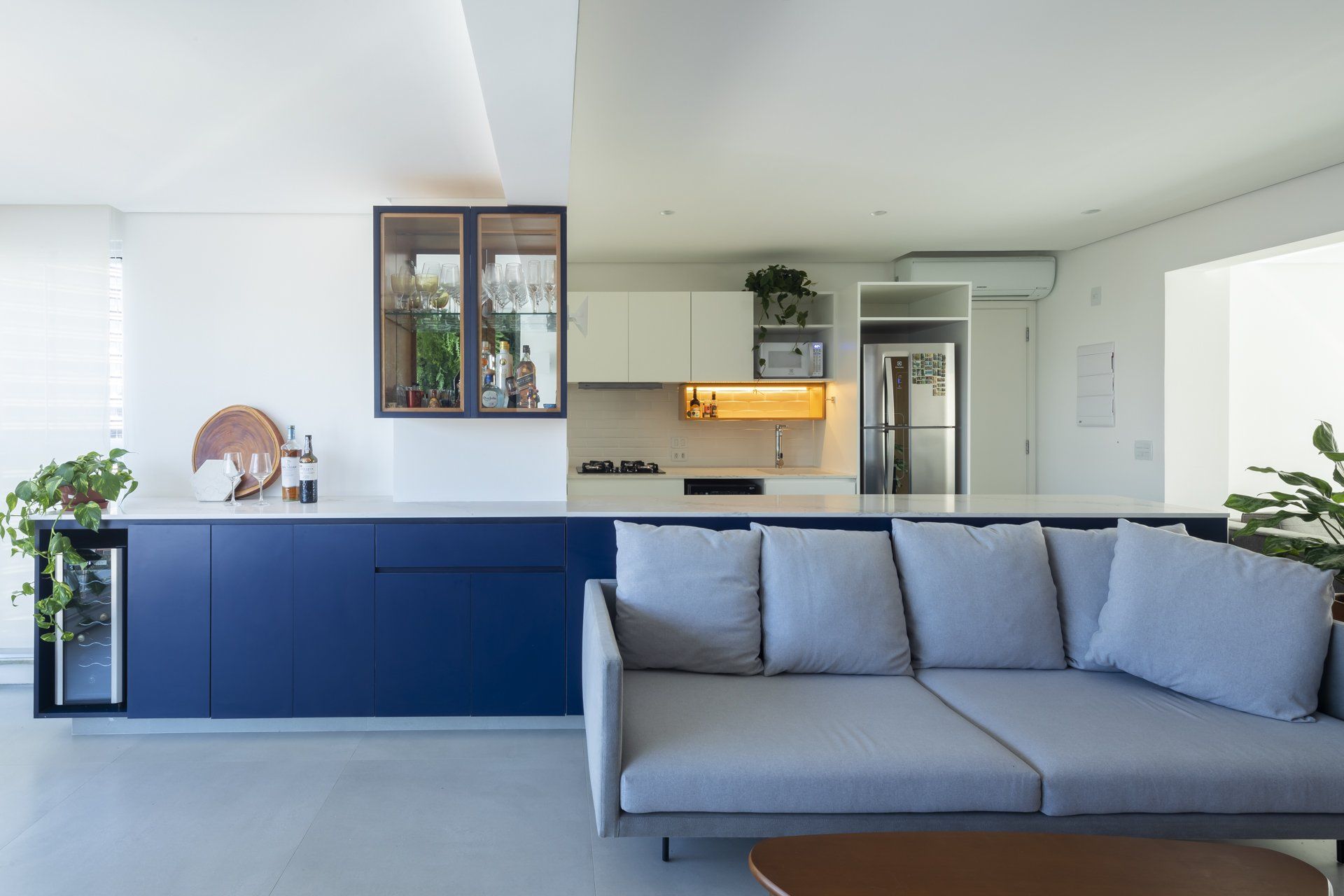 Uma sala com sofá e uma cozinha ao fundo.