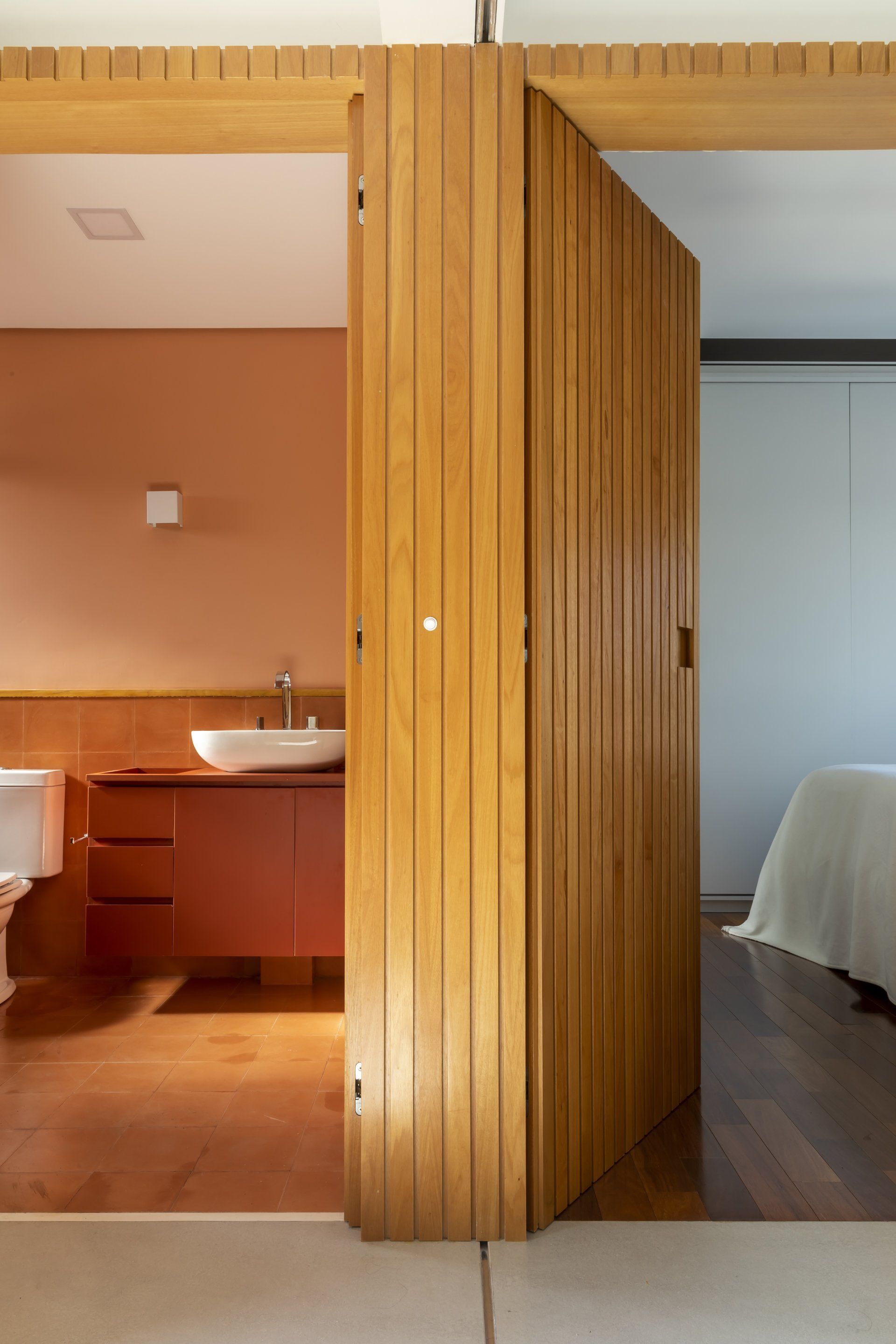 Uma porta de madeira está aberta para um banheiro e um quarto.