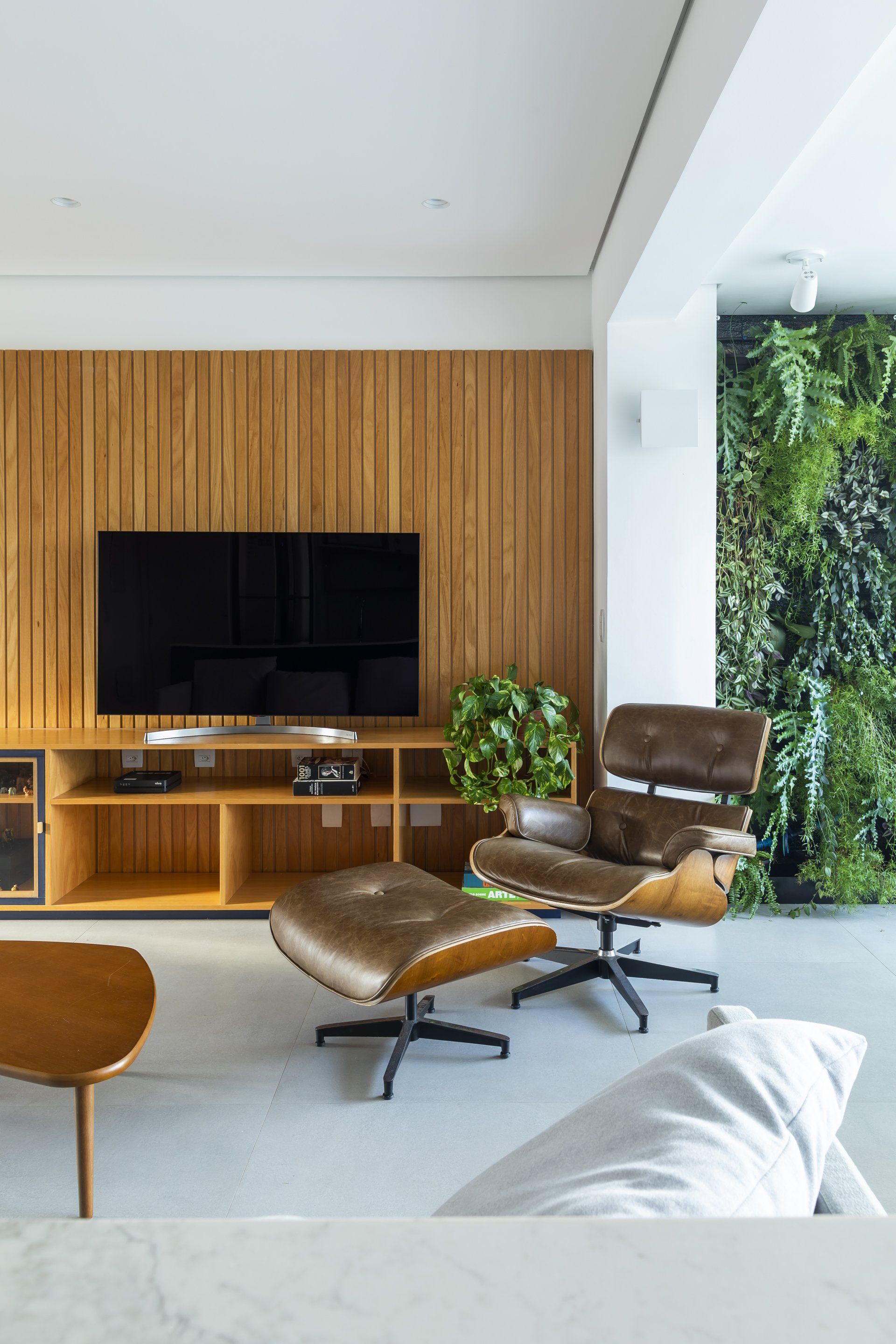 Uma sala com cadeira, pufe, televisão e parede de madeira.