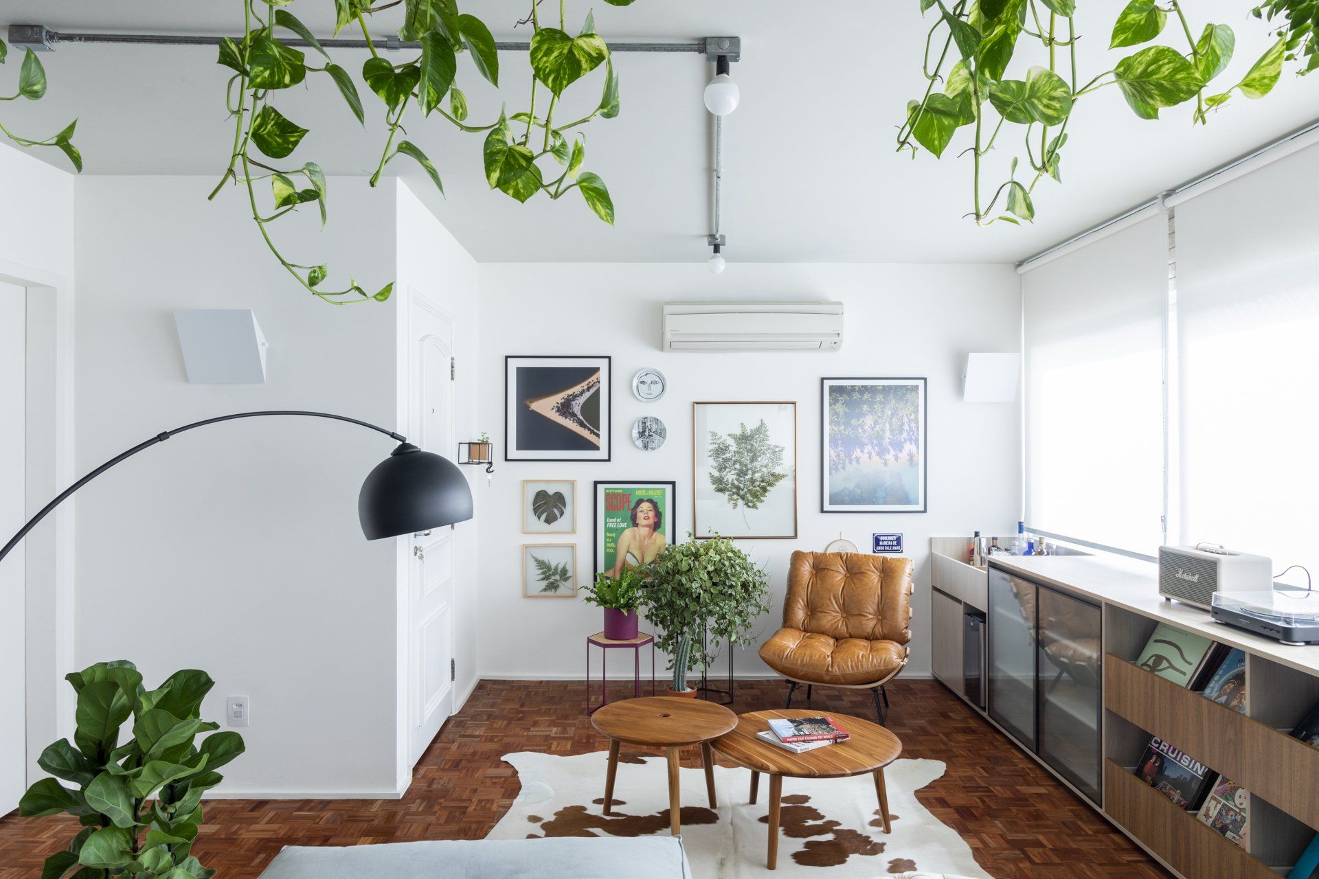 Uma sala com sofá, cadeira, mesas e plantas.