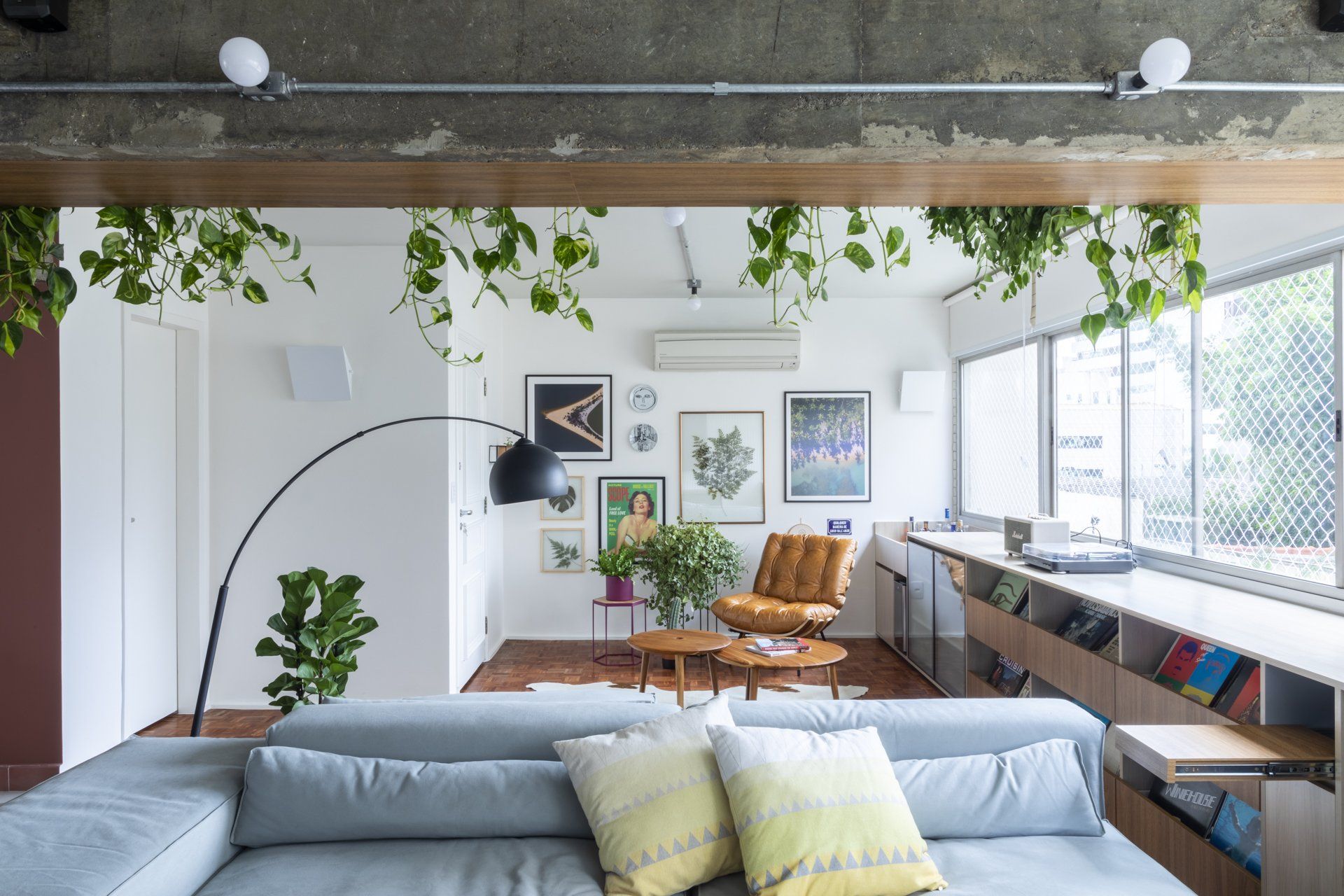 Uma sala com sofá, cadeira, mesa e plantas penduradas no teto.