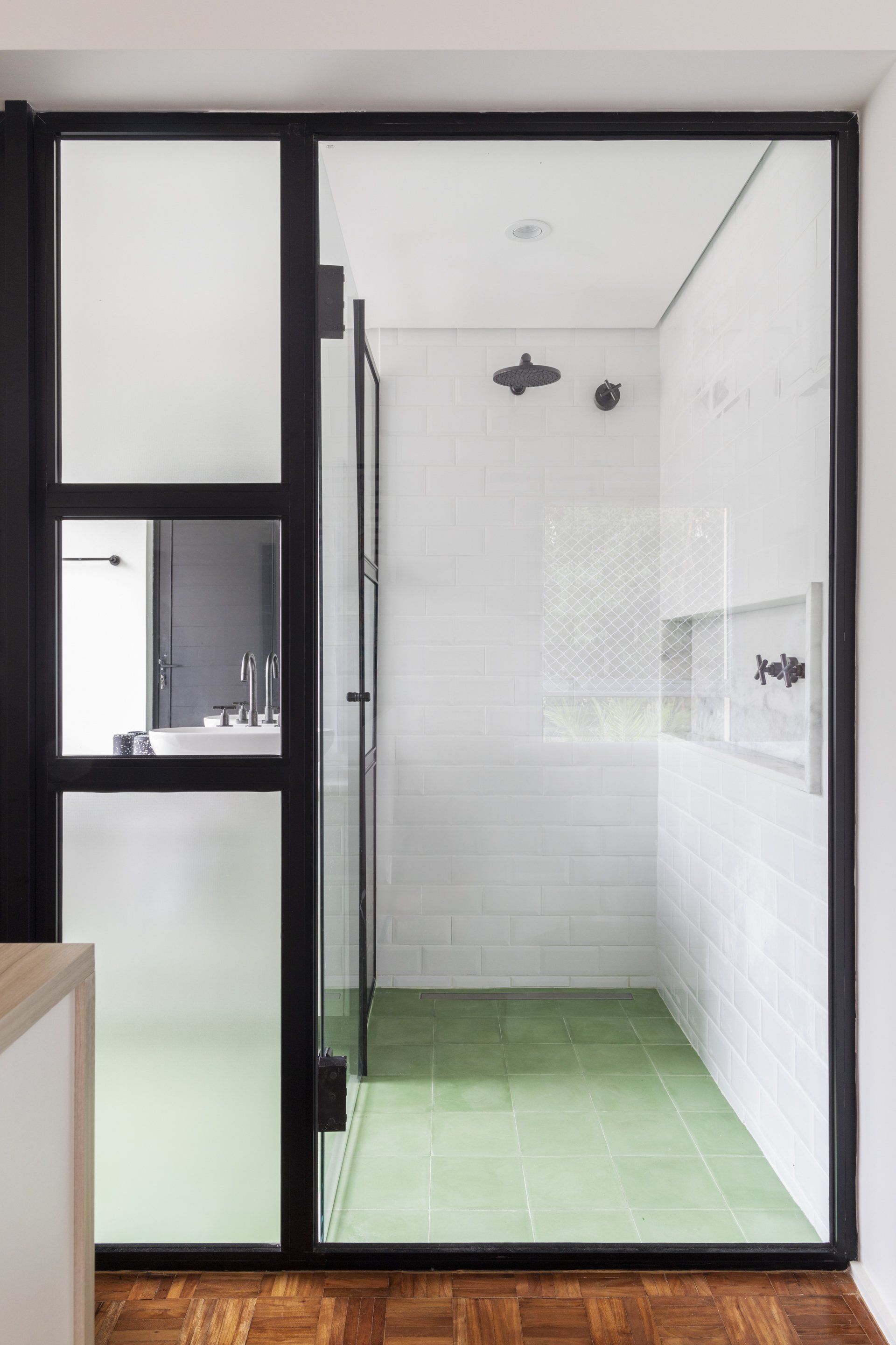 Uma casa de banho com chão em mosaico verde e porta de vidro.